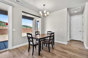 Dining area featuring wood-finish flooring, a contemporary chandelier, light gray wall paint, and a sliding glass door leading to an outdoor space