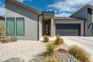 Contemporary stucco exterior with a multi-pane front door, attached two-car garage, stone accents, and xeriscape landscaping