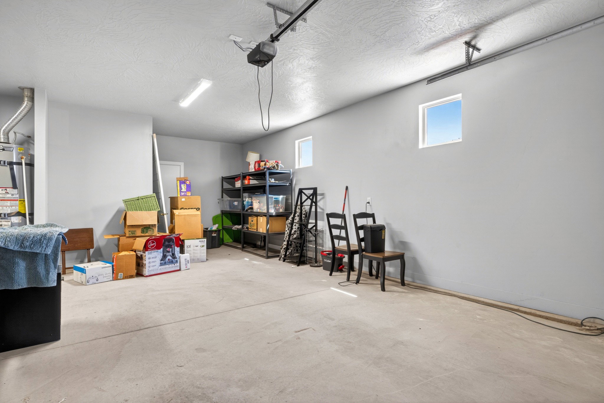 Spacious garage with concrete flooring, high ceilings, two rectangular windows, and overhead lighting
