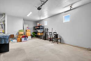 Spacious garage with concrete flooring, high ceilings, two rectangular windows, and overhead lighting