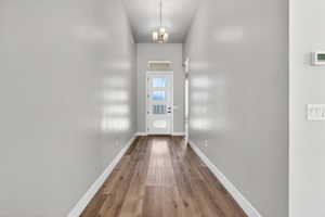 Entryway featuring wood-finish flooring, light grey walls, and a recessed ceiling with a chandelier