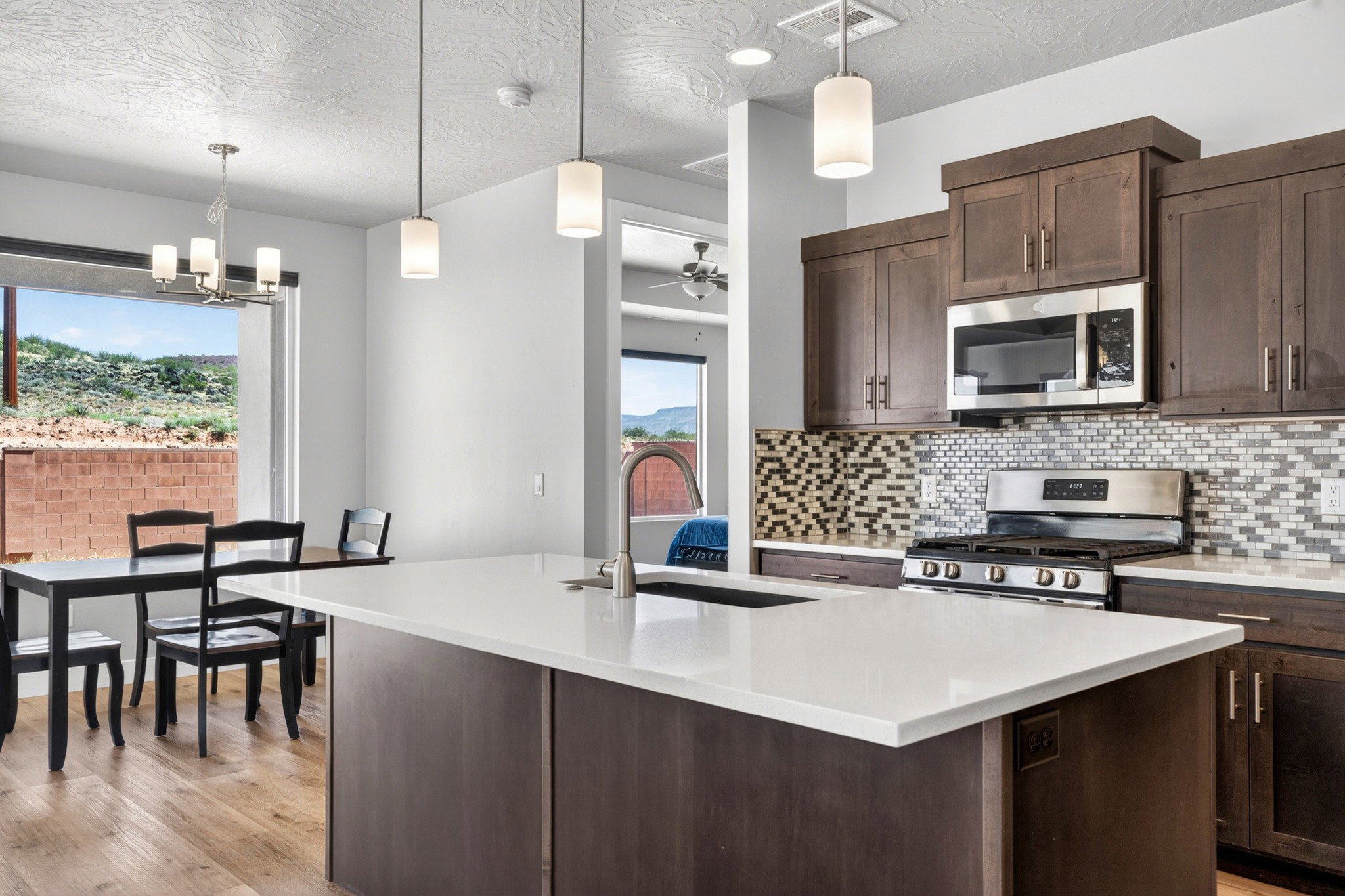 Open-concept kitchen featuring a large island with white countertop, dark wood cabinetry, stainless steel appliances, and a mosaic tile backsplash