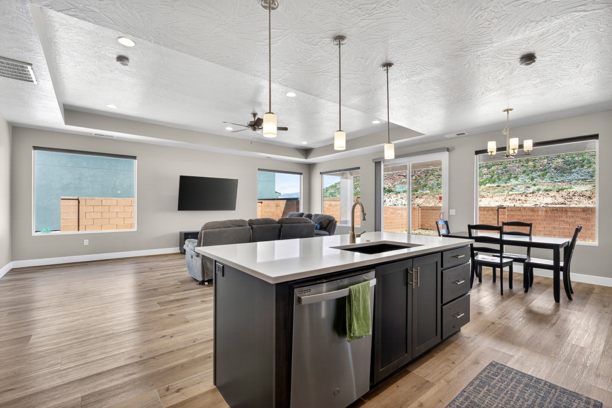 Open-concept living space featuring wood-finish flooring, a kitchen island with a white countertop and dark cabinetry, and multiple windows