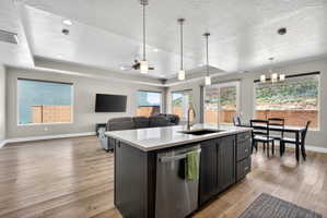 Open-concept living space featuring wood-finish flooring, a kitchen island with a white countertop and dark cabinetry, and multiple windows