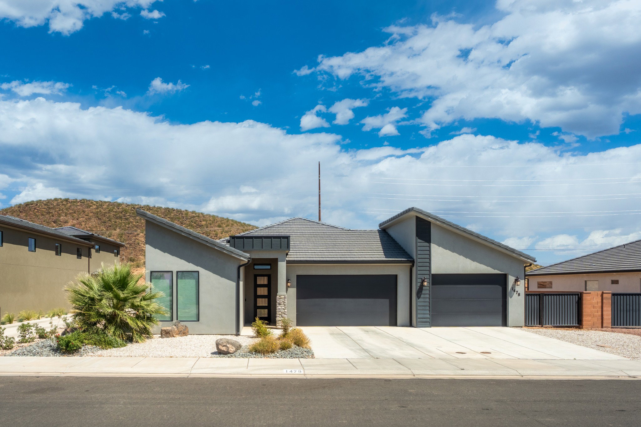 Modern exterior featuring a prominent two-car garage, low-slope rooflines, a distinct entry door with vertical glass inserts, and a desert-inspired landscape with natural rock elements