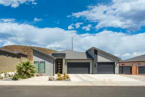 Modern exterior featuring a prominent two-car garage, low-slope rooflines, a distinct entry door with vertical glass inserts, and a desert-inspired landscape with natural rock elements