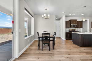 Open-concept dining area featuring wood-finish flooring, a modern chandelier, and ample natural light from the large window and sliding glass door