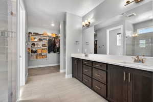 Spacious bathroom featuring light-toned tile flooring, a dual-sink vanity with dark wood cabinetry and white countertops, a large wall-mounted mirror with overhead lighting, and a walk-in shower with clear glass enclosure