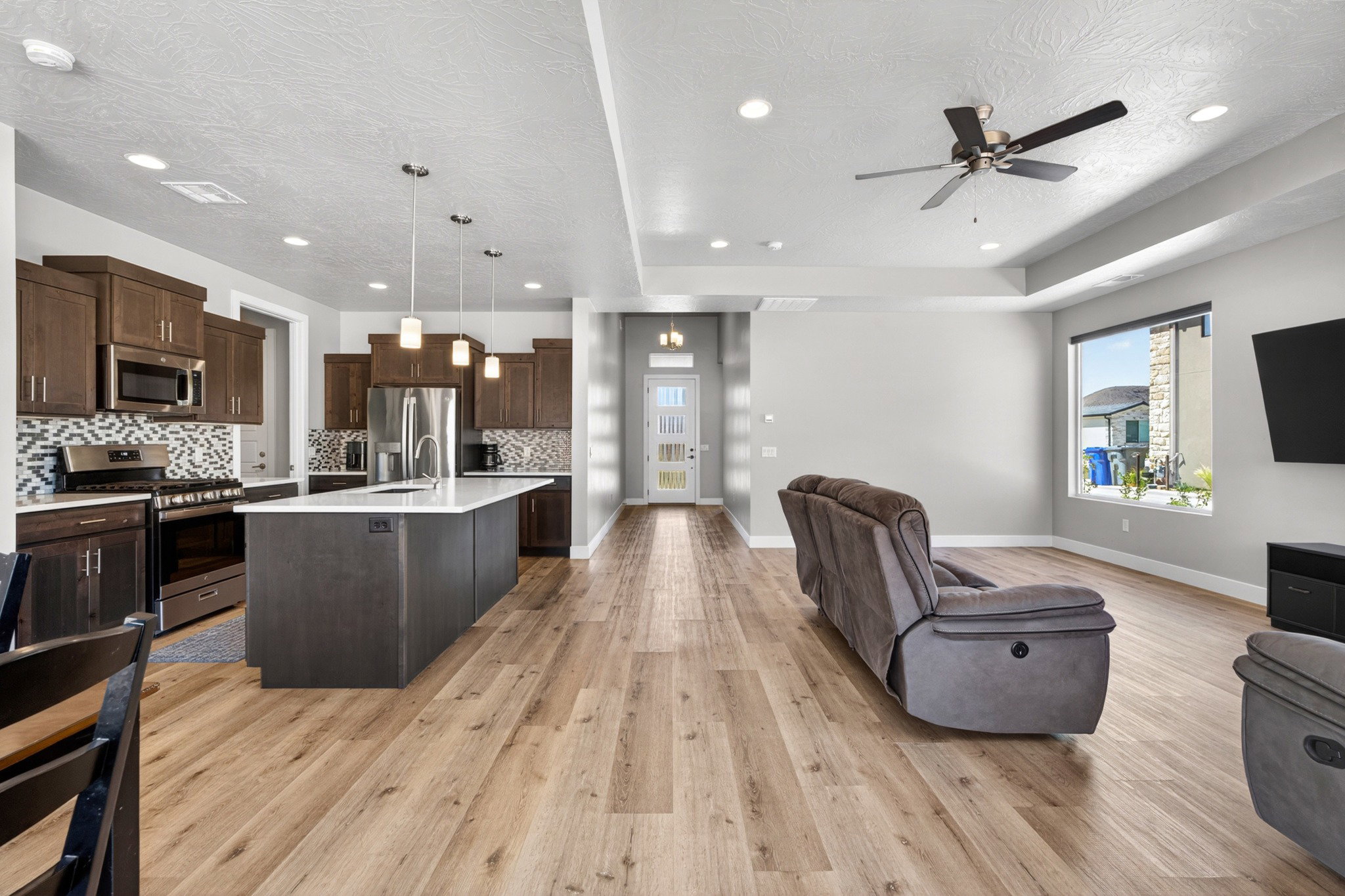 Open-concept kitchen and living area featuring wood-finish flooring, recessed lighting, and a contemporary ceiling fan