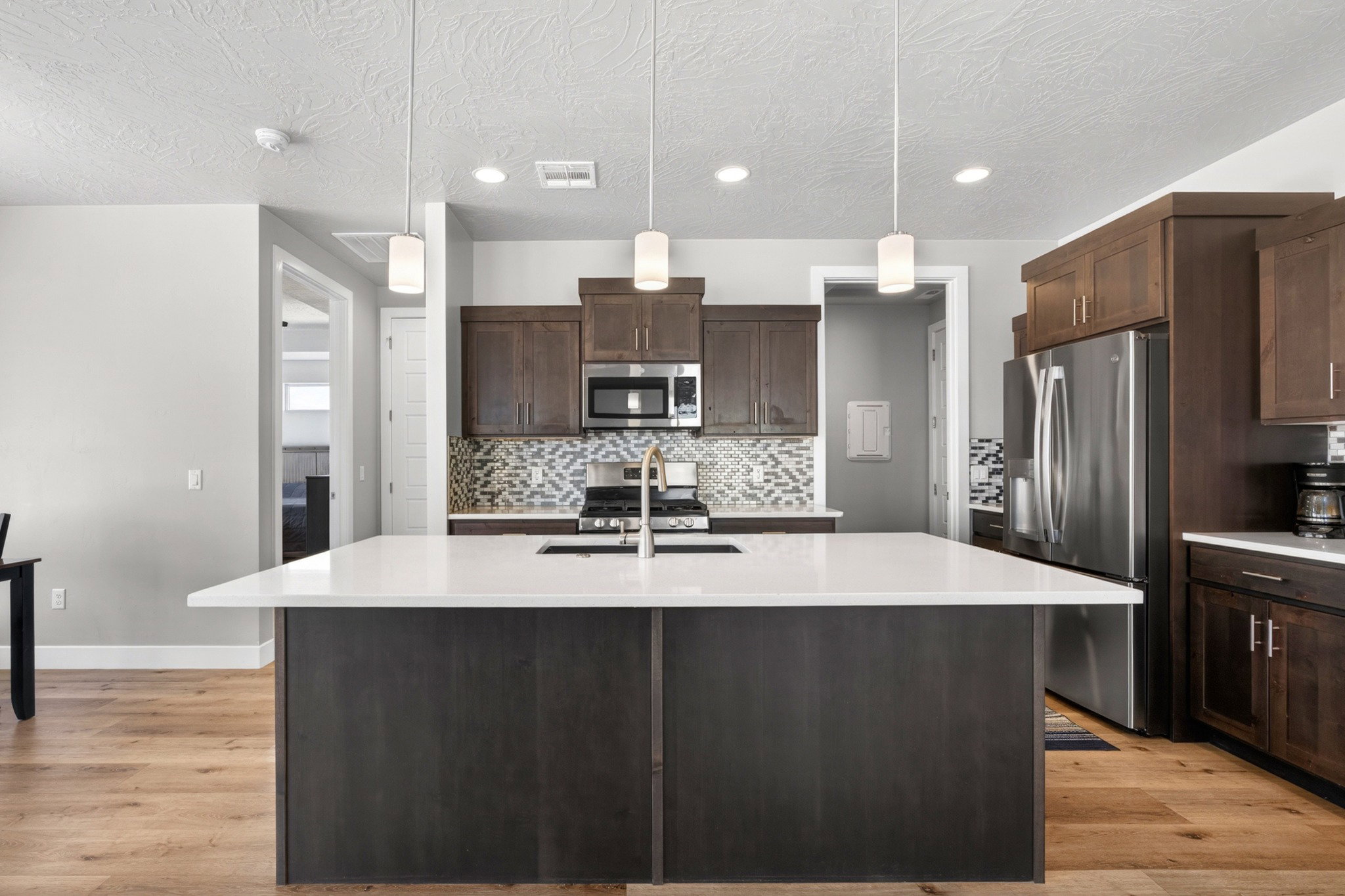 Kitchen featuring a large central island with white countertop, dark wood-finish cabinetry, stainless steel appliances, and wood-finish flooring