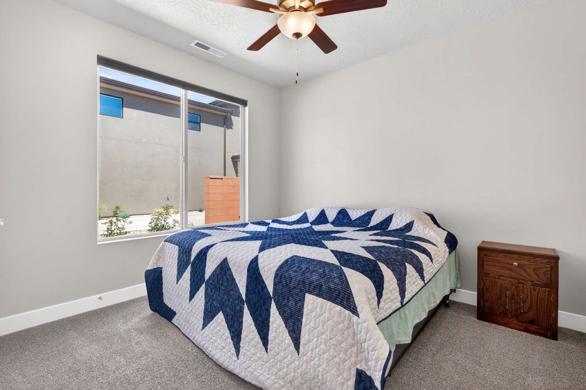 Carpeted room featuring a large window, a ceiling fan with integrated lighting, and neutral wall paint