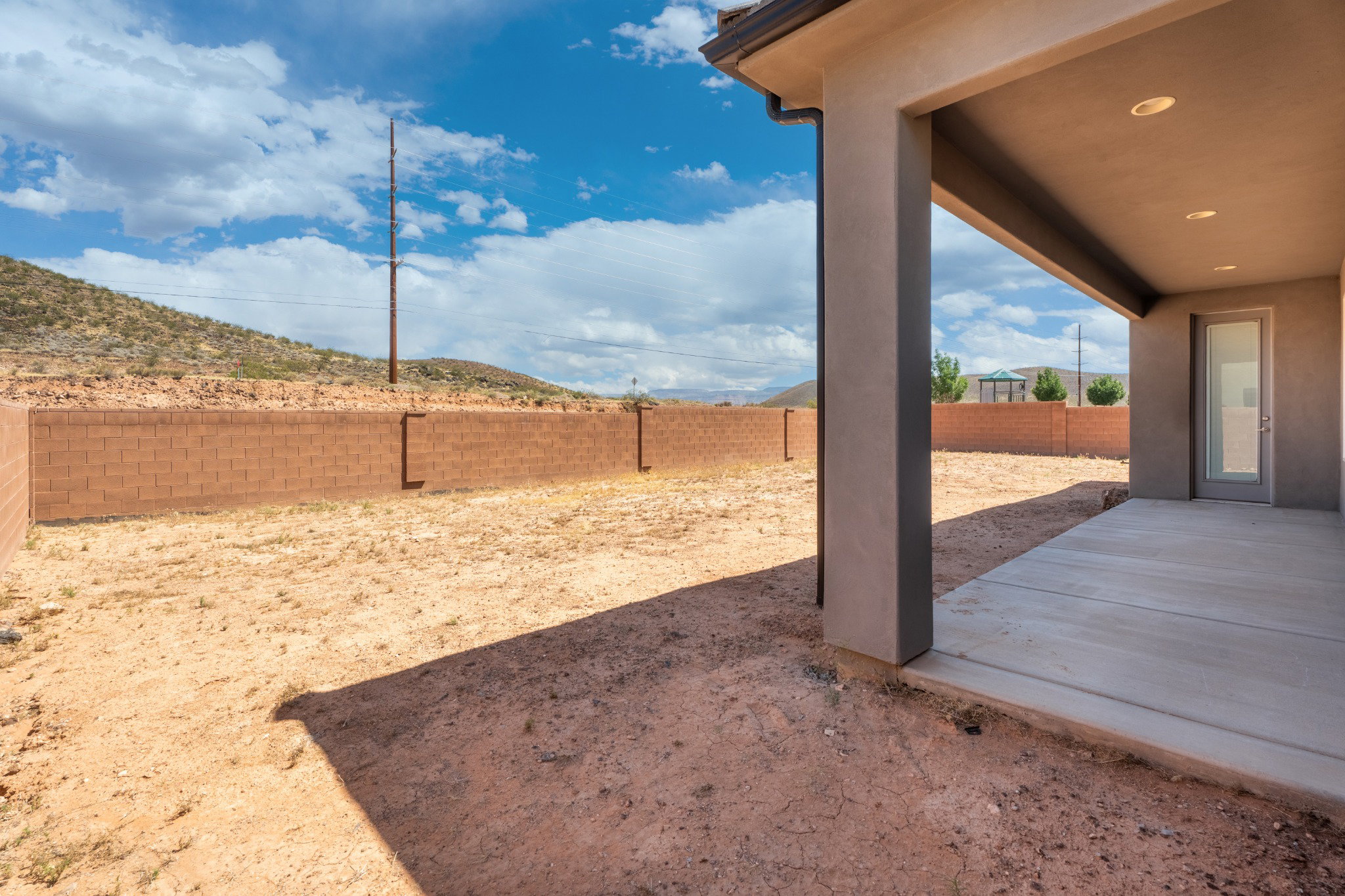 Expansive backyard featuring a concrete patio, stucco overhang with recessed lighting, and a full-height block wall perimeter