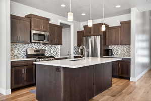 Contemporary kitchen featuring dark wood cabinetry, stainless steel appliances, a mosaic tile backsplash, and a central island with a white countertop