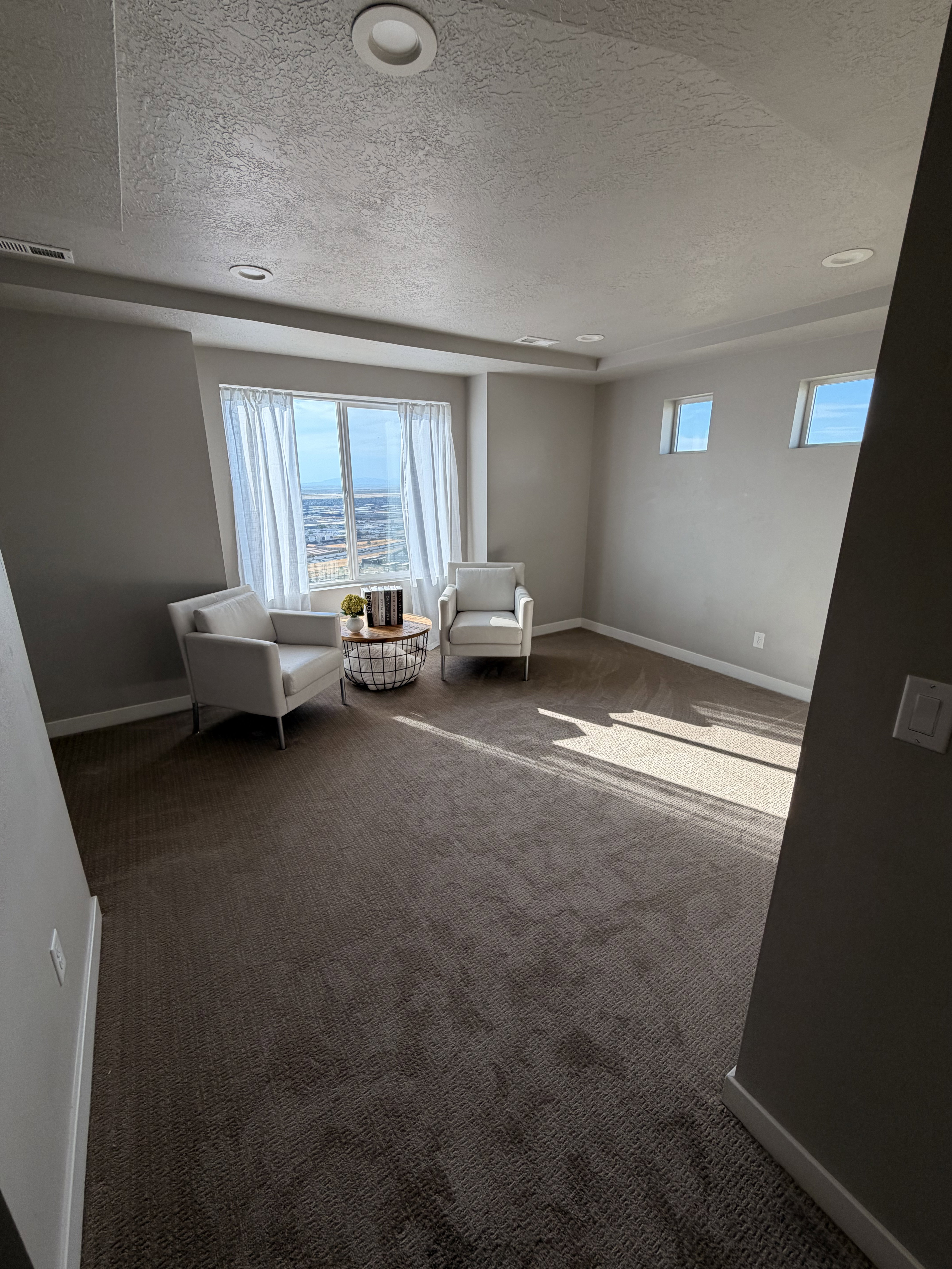 Spacious room featuring broadloom carpet, recessed lighting, a large picture window with white drapery, and additional rectangular windows providing natural light