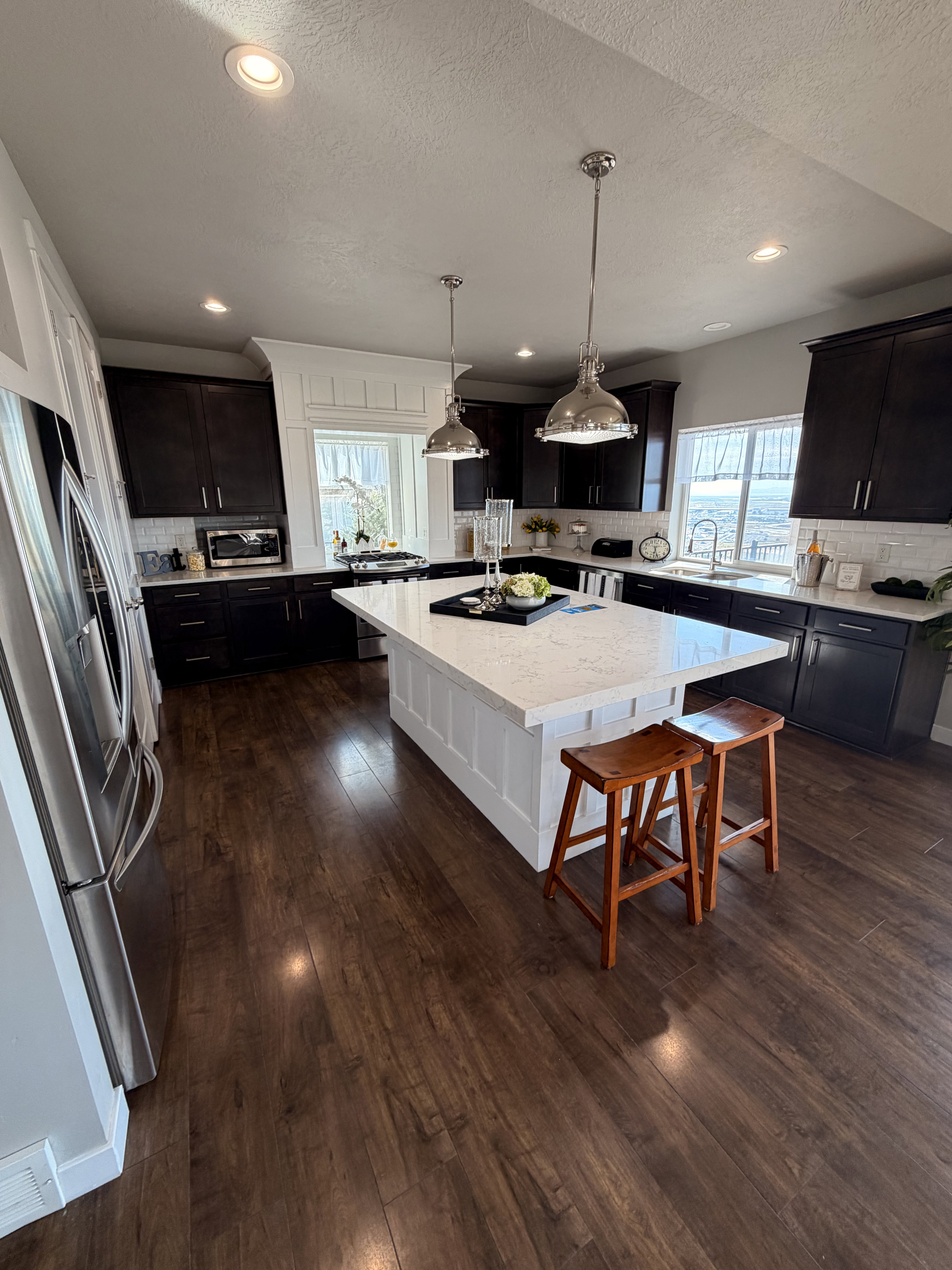 Spacious kitchen featuring a large white center island with a light-colored countertop, dark wood-finish cabinetry, stainless steel appliances, and wood-finish flooring