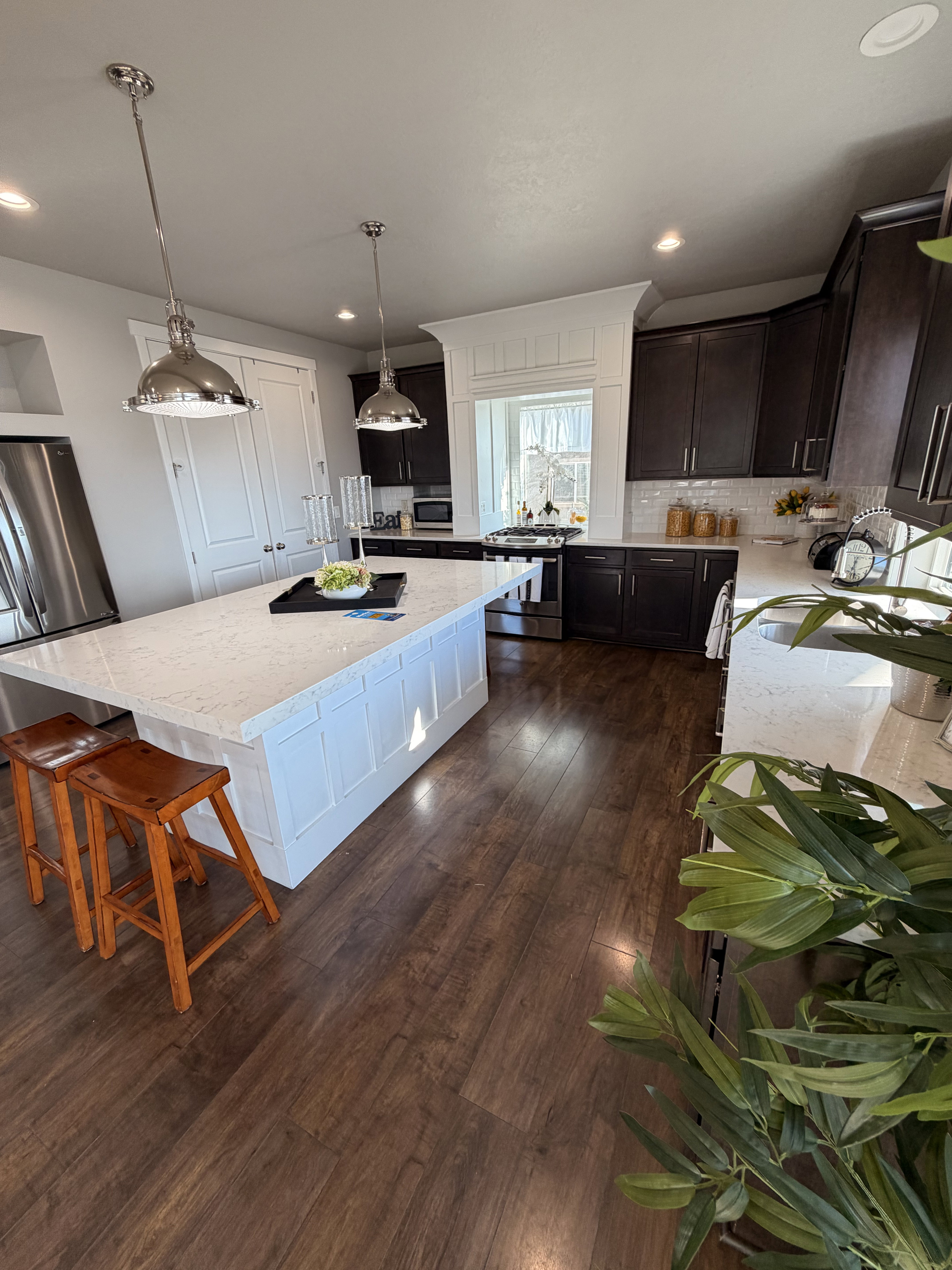 Open-concept kitchen featuring an oversized island with white paneled cabinetry, light-toned countertops, and two polished pendant lights