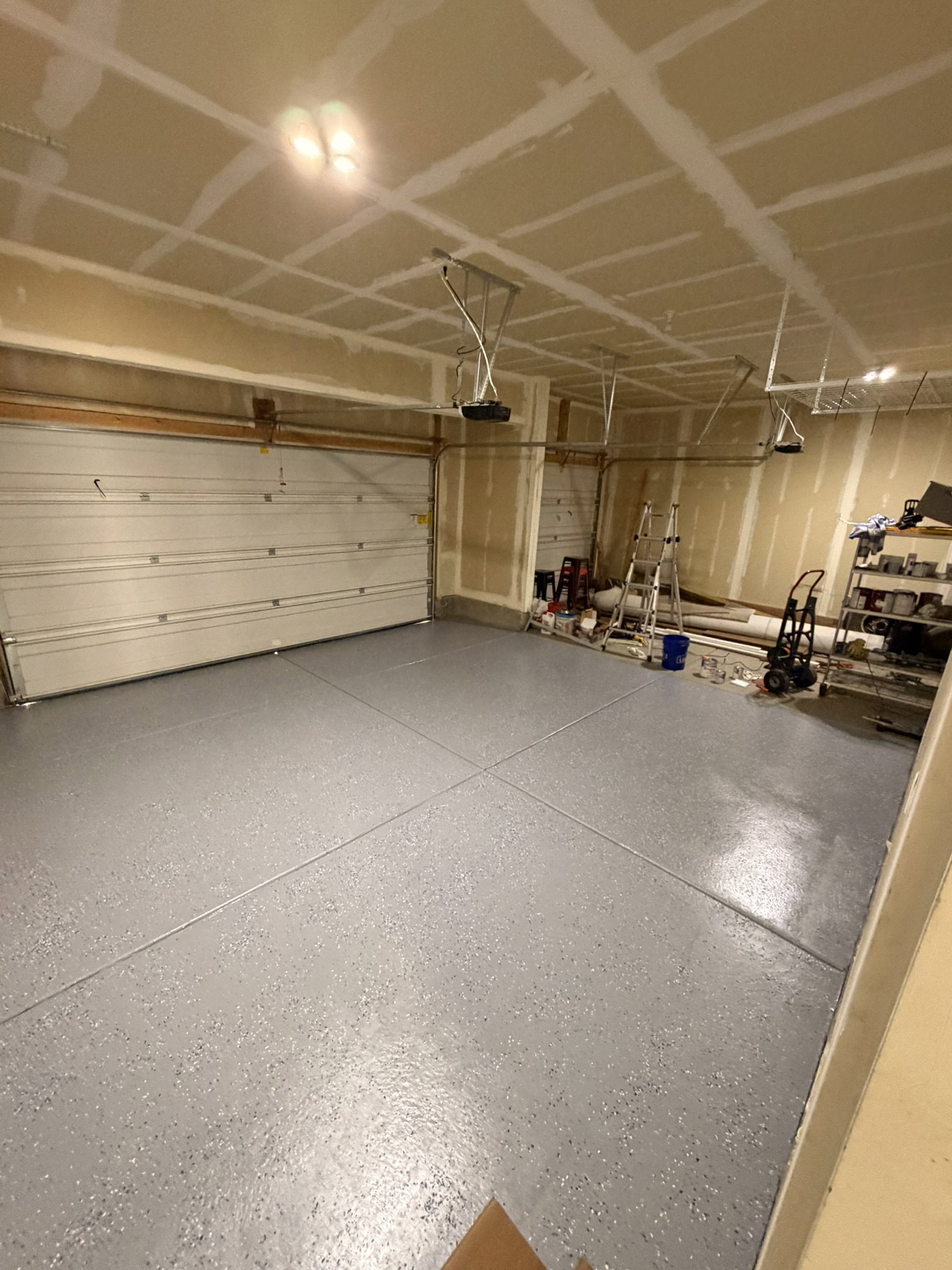 Spacious garage featuring a durable epoxy-coated floor, two overhead garage doors, and multiple ceiling-mounted light fixtures