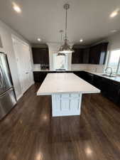 Kitchen featuring a large central island with a light-toned countertop, dark wood-finish cabinetry, and stainless steel appliances
