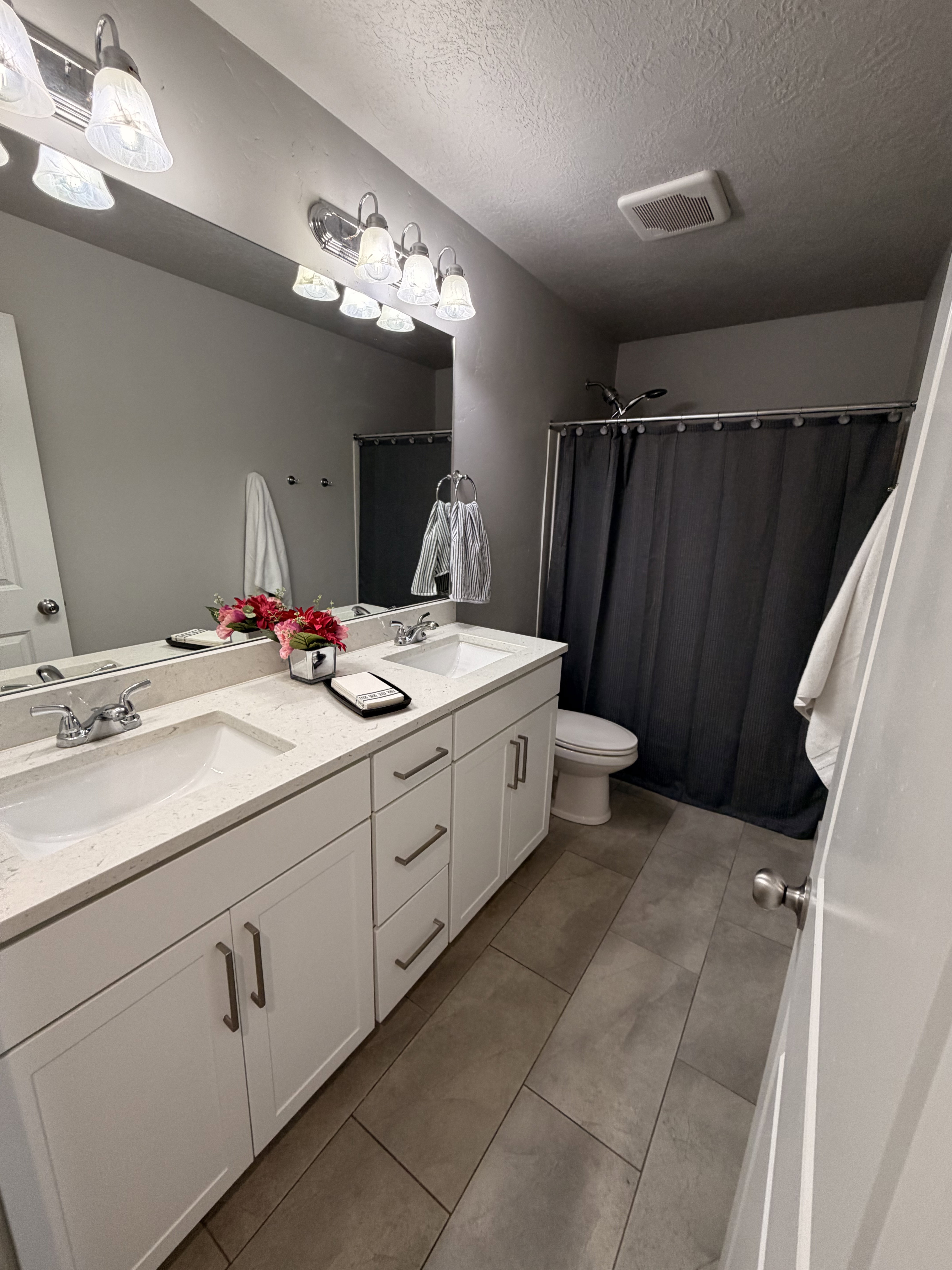 Spacious bathroom featuring a dual vanity with white cabinetry, light-toned countertops, and two undermount sinks