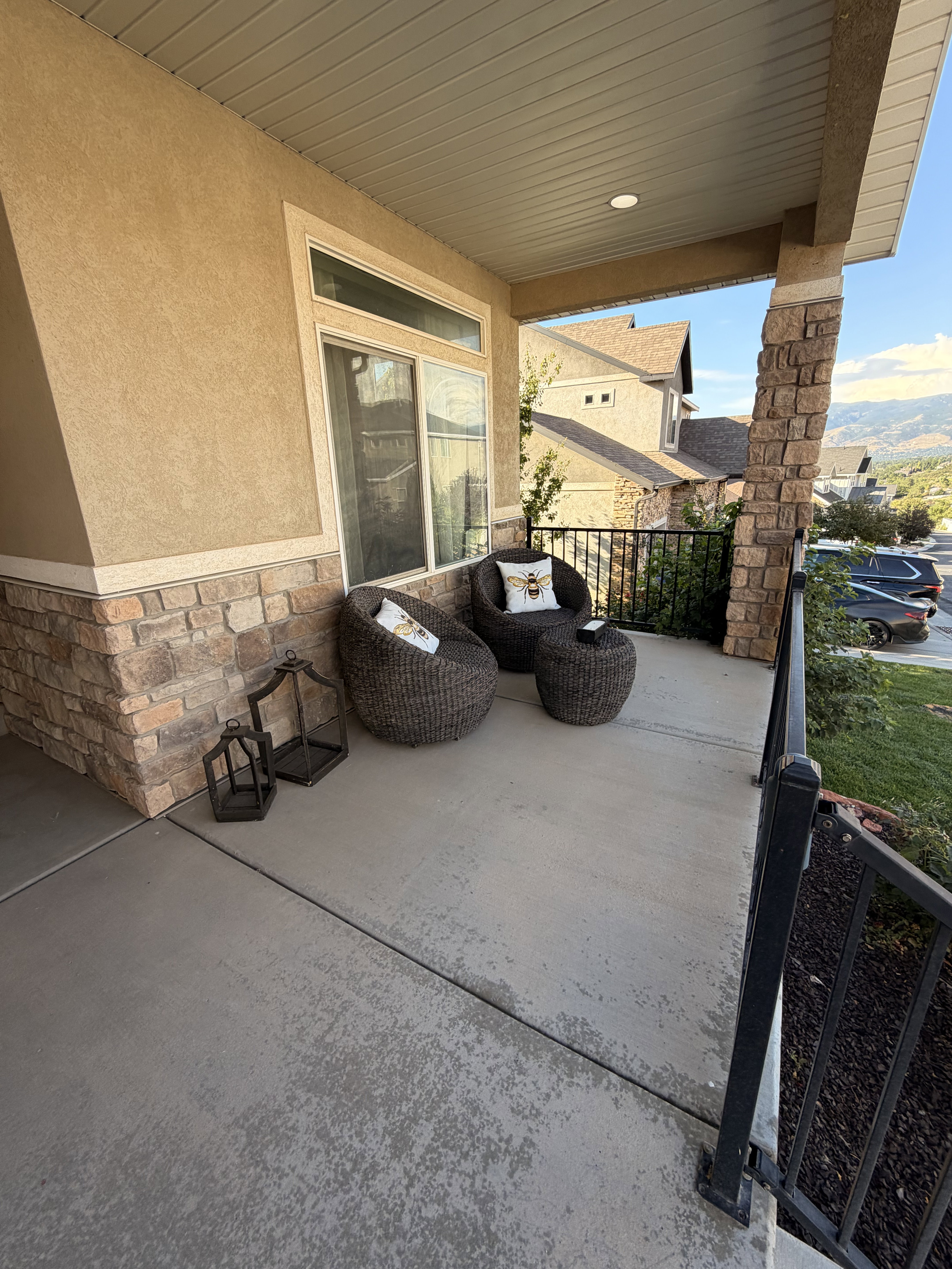 Covered concrete patio with stone veneer facade, stucco exterior, and black metal railing