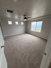 Spacious room featuring a tray ceiling with a ceiling fan, plush carpet flooring, and multiple windows including a large picture window
