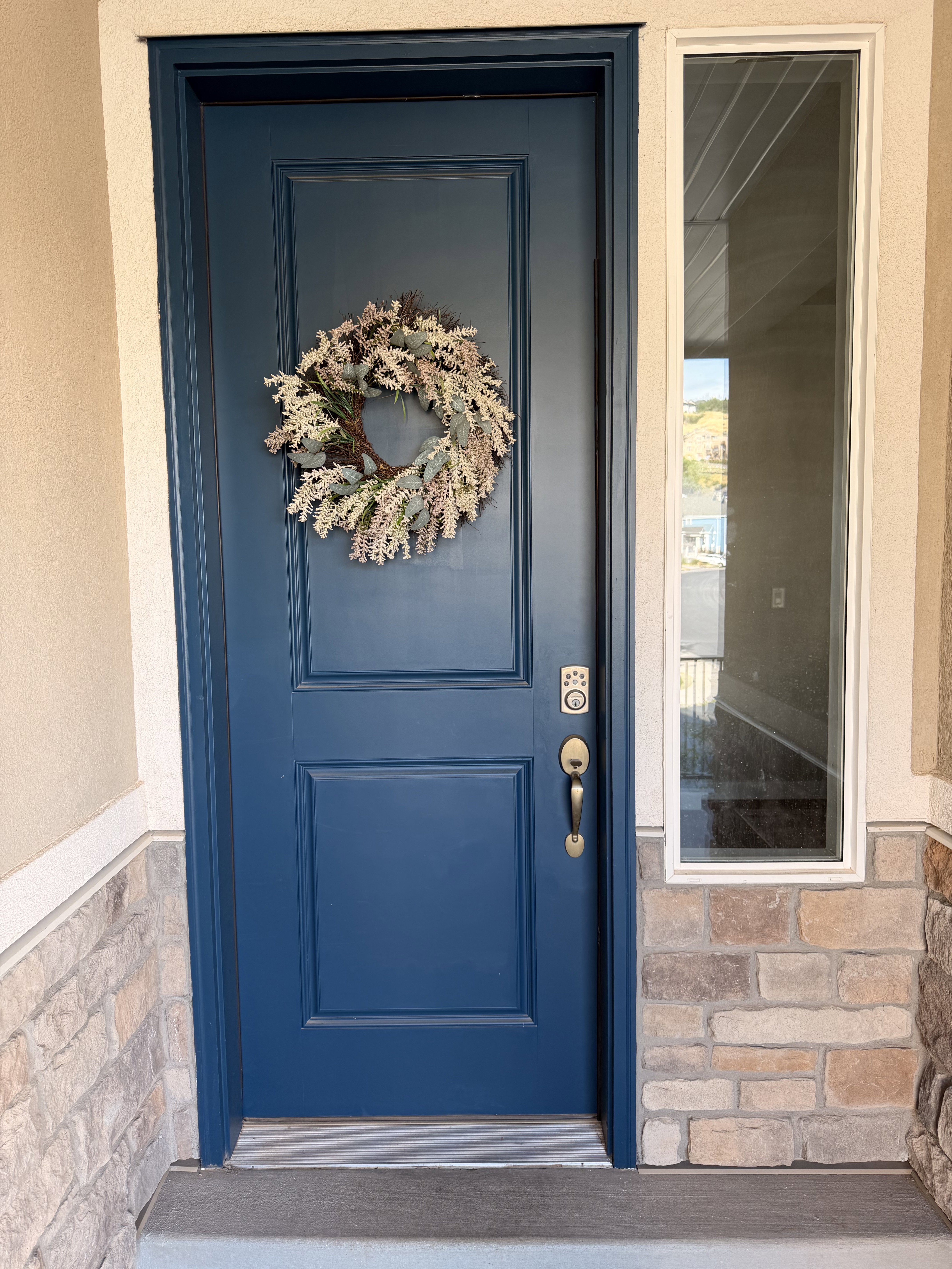 Blue paneled door with a brass handle and a digital keypad lock, complemented by a vertical sidelight window