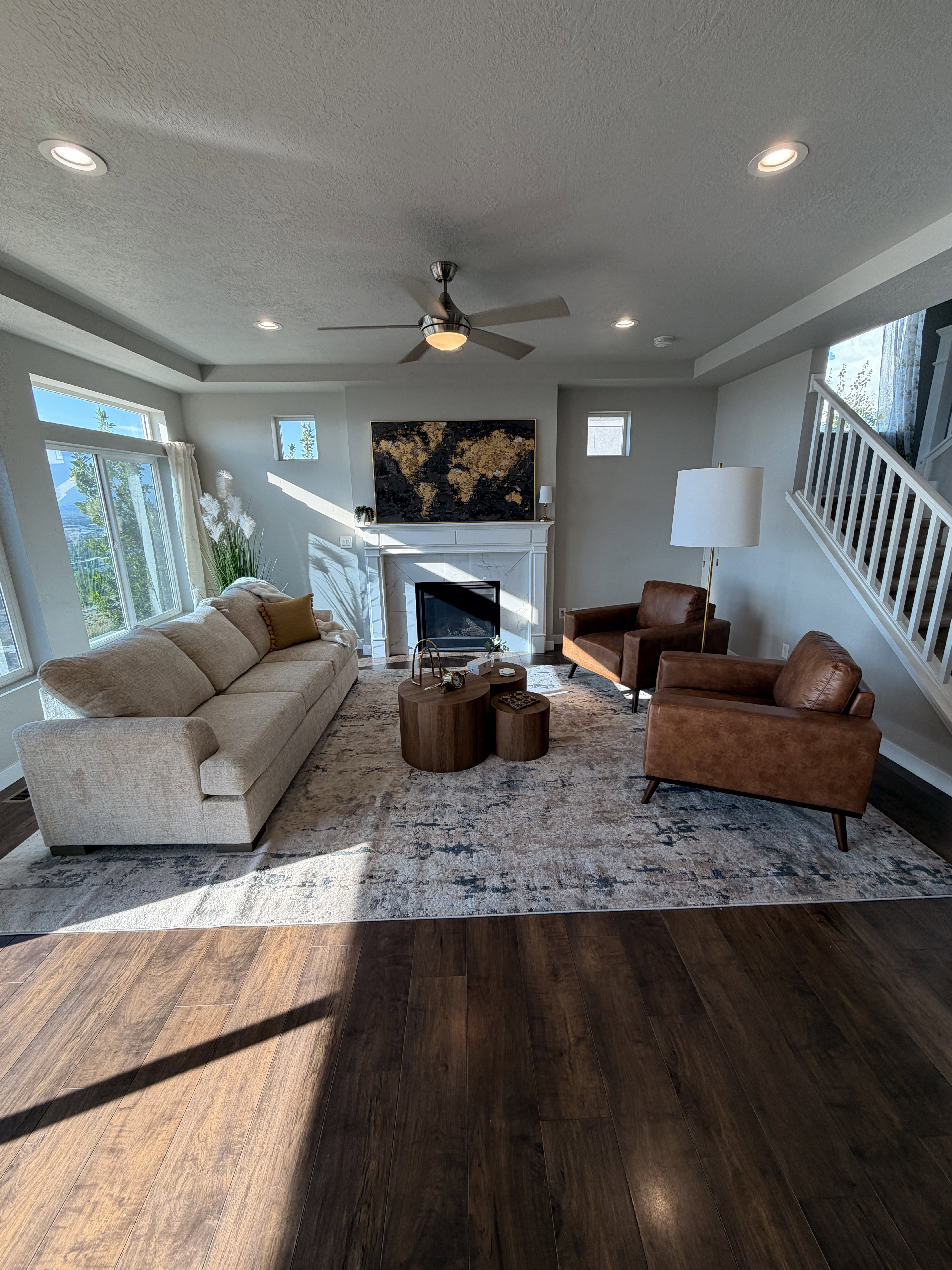 Spacious living area featuring wood-finish flooring, a contemporary ceiling fan, recessed lighting, a white mantel fireplace, and a light-toned staircase with white balusters