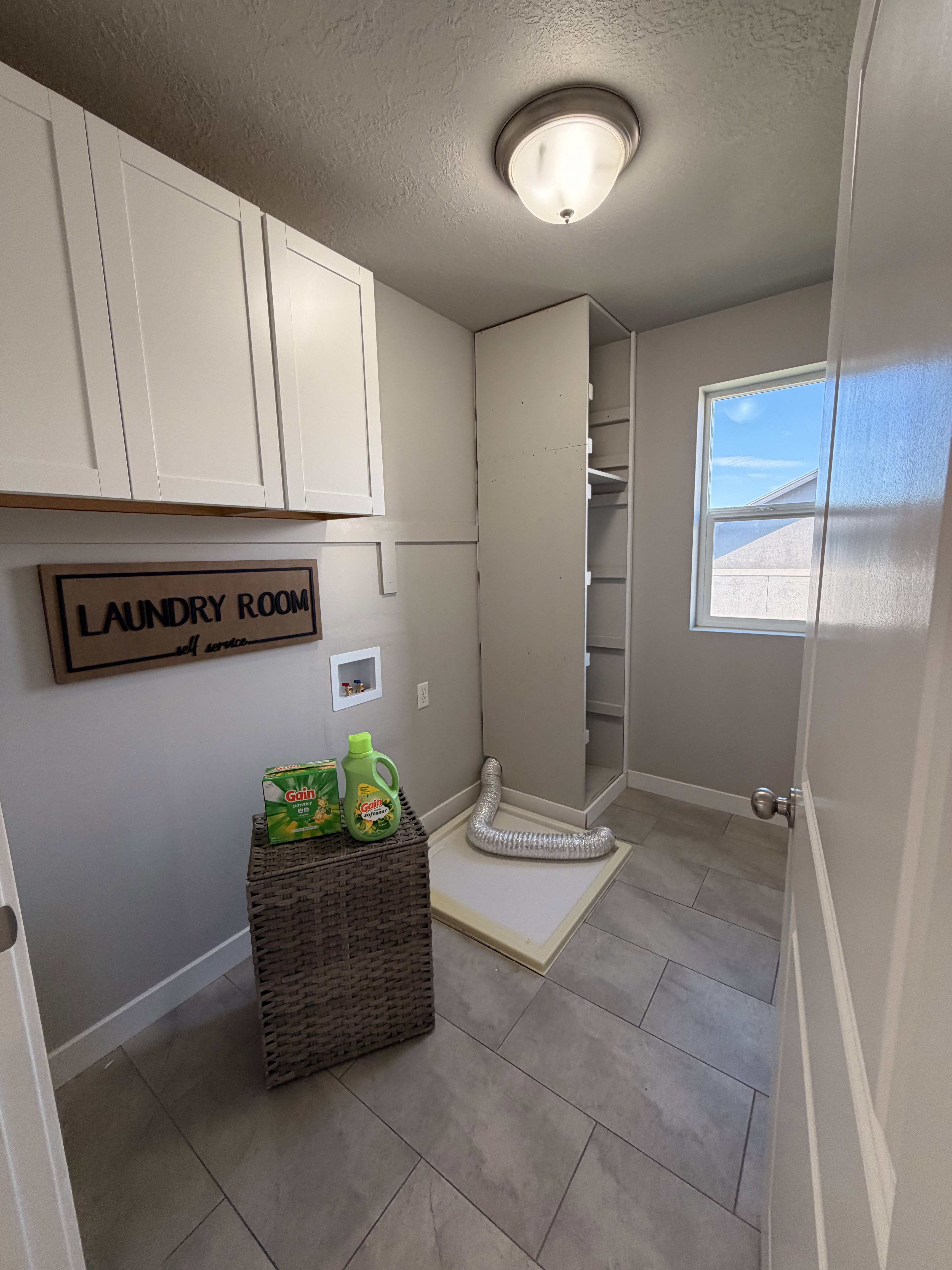 Laundry room featuring white shaker-style cabinetry, built-in shelving, a single window, and a tile floor