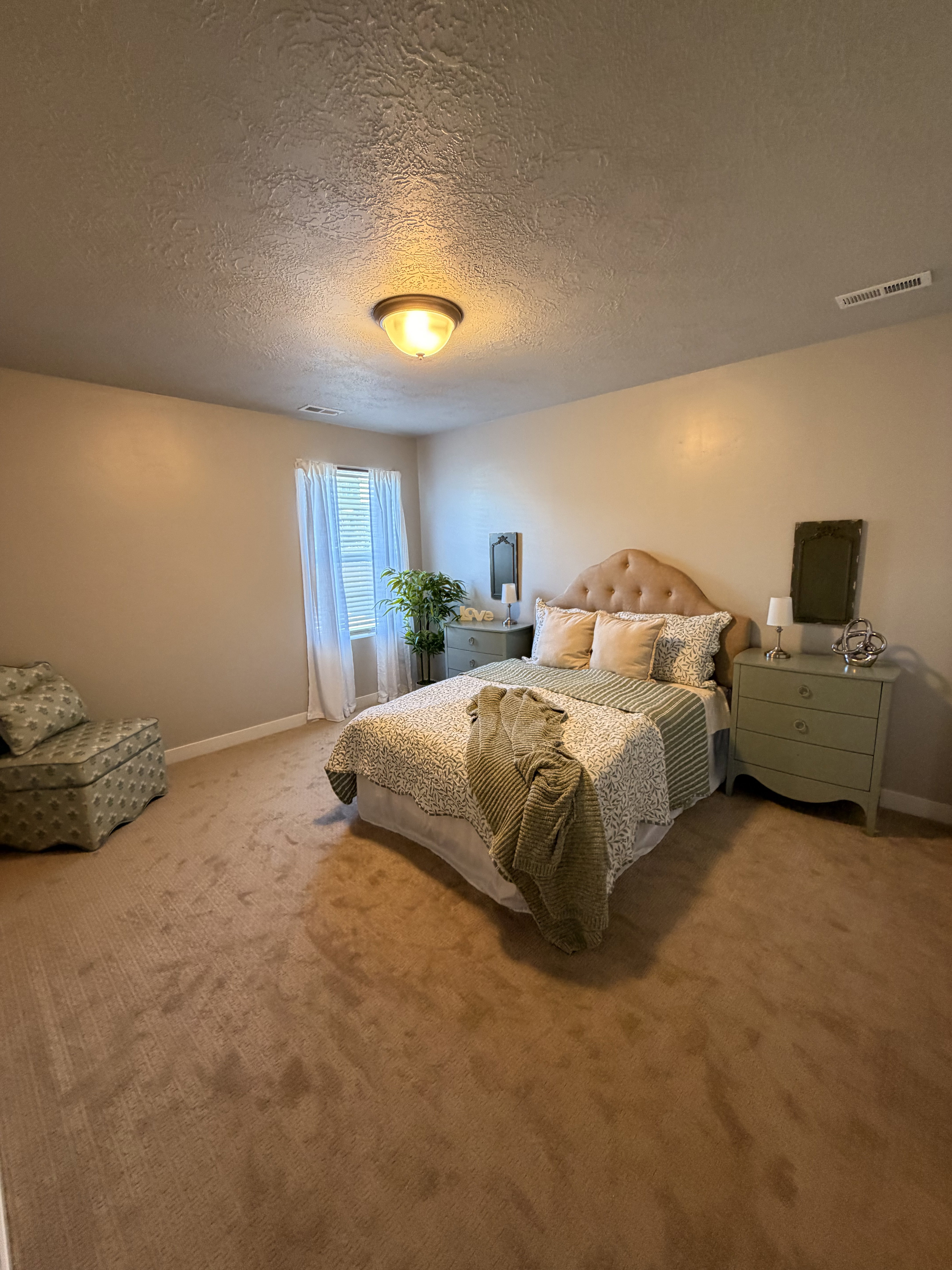 Carpeted room featuring a window with white drapes, a textured ceiling, and a flush mount light fixture