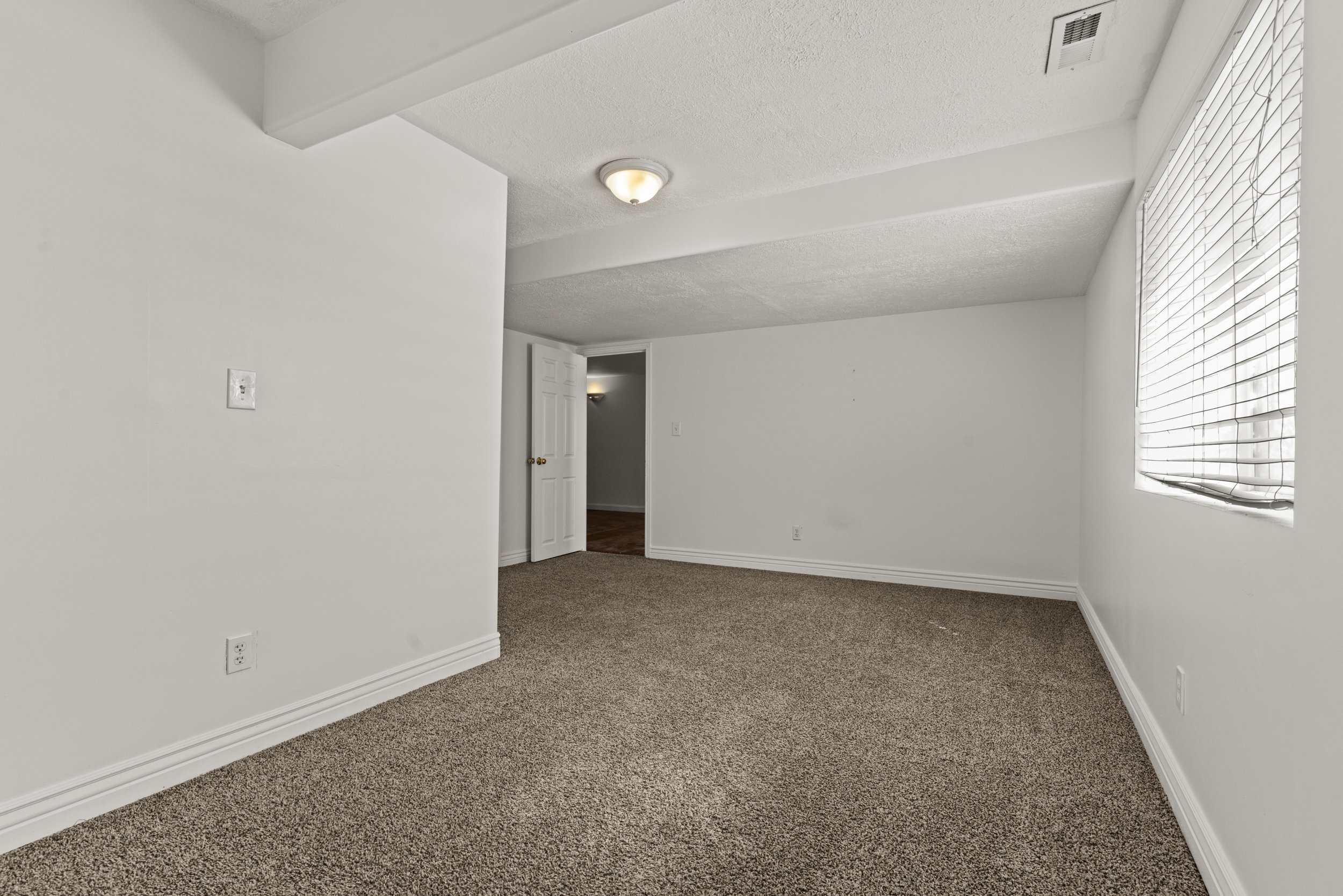 Carpeted interior room featuring white painted walls, white trim, and a window with horizontal blinds
