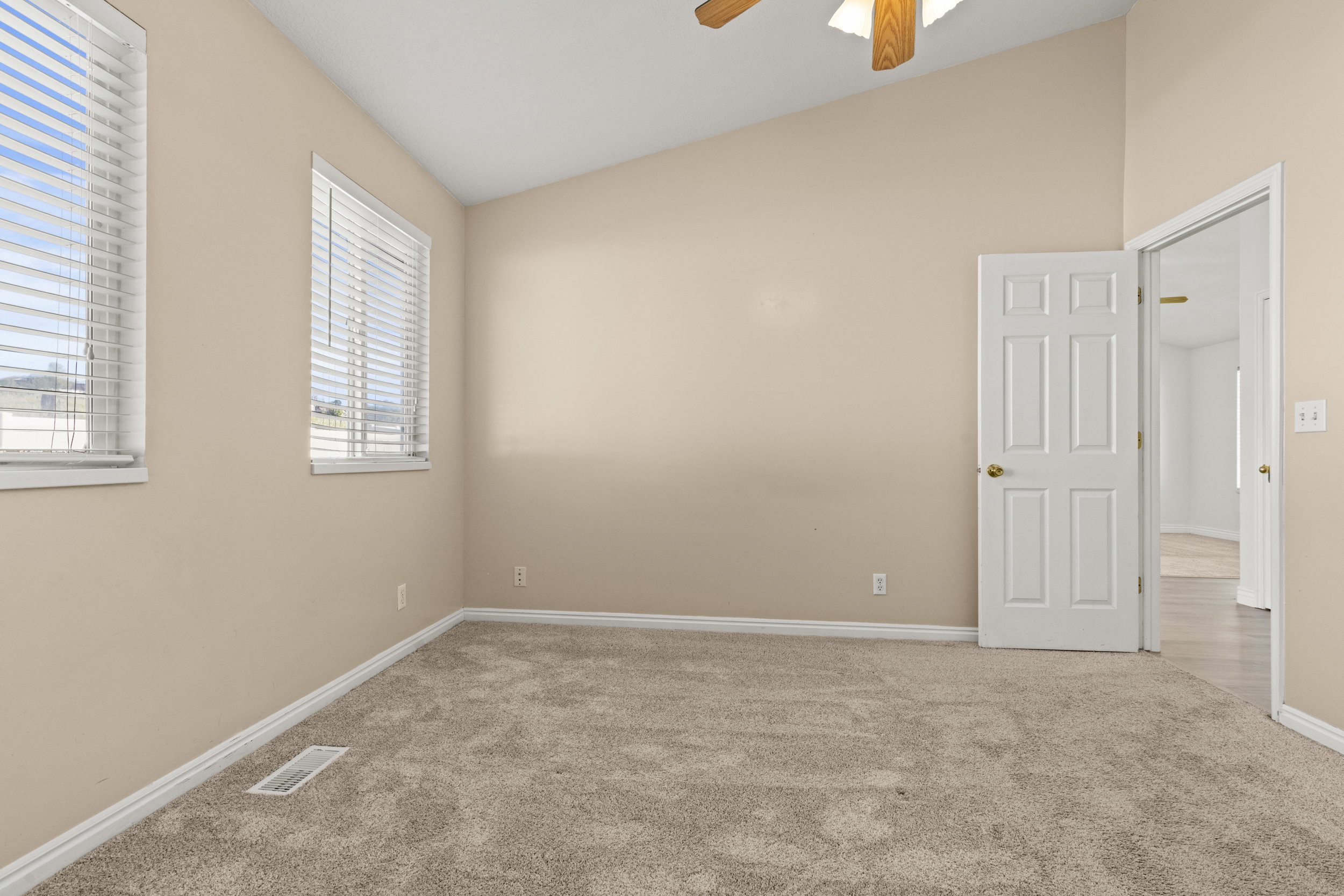 Carpeted interior room featuring a vaulted ceiling with a ceiling fan, two windows with blinds, and light neutral wall tones