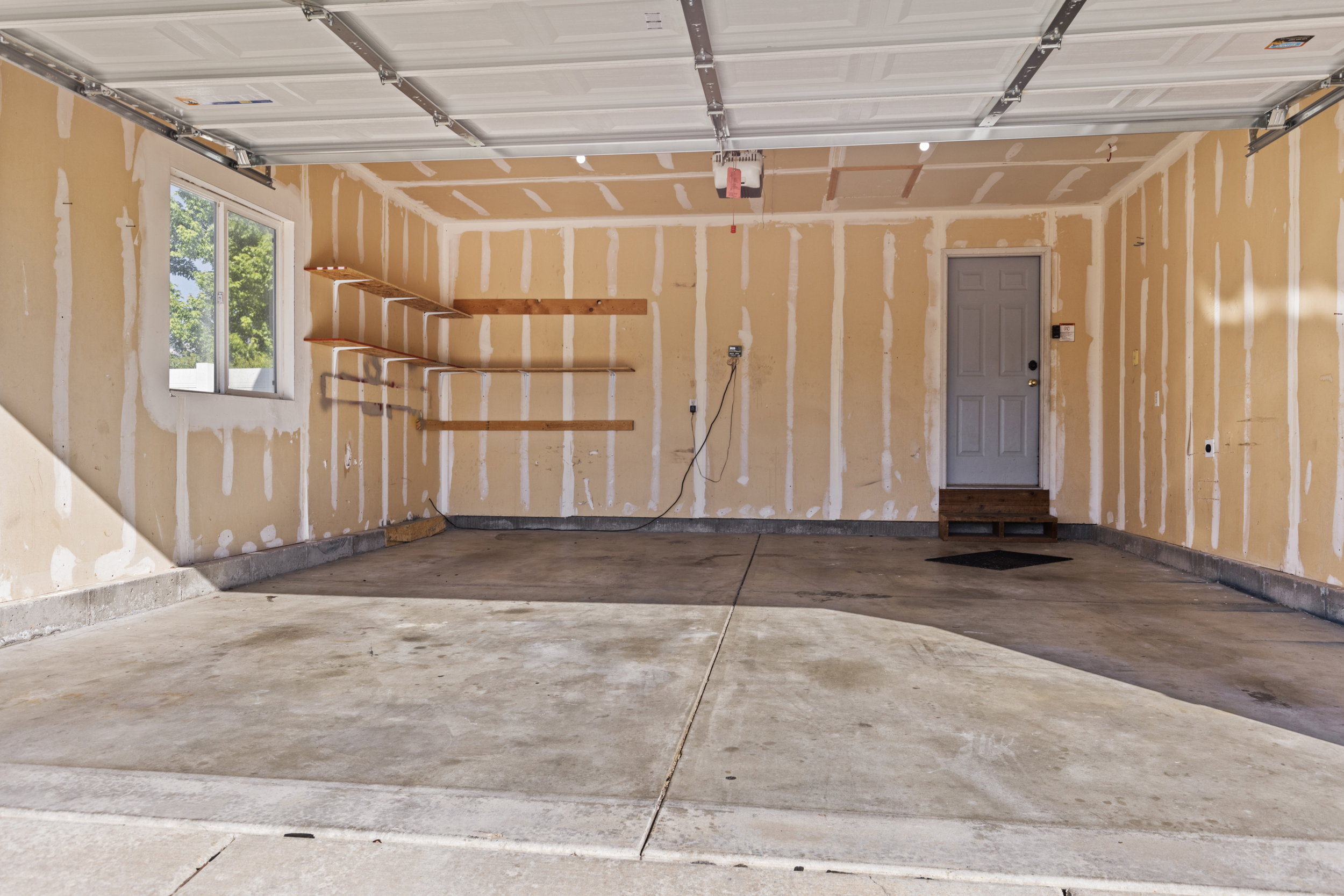 Garage interior featuring a concrete floor, built-in shelving, a single window, and an interior access door