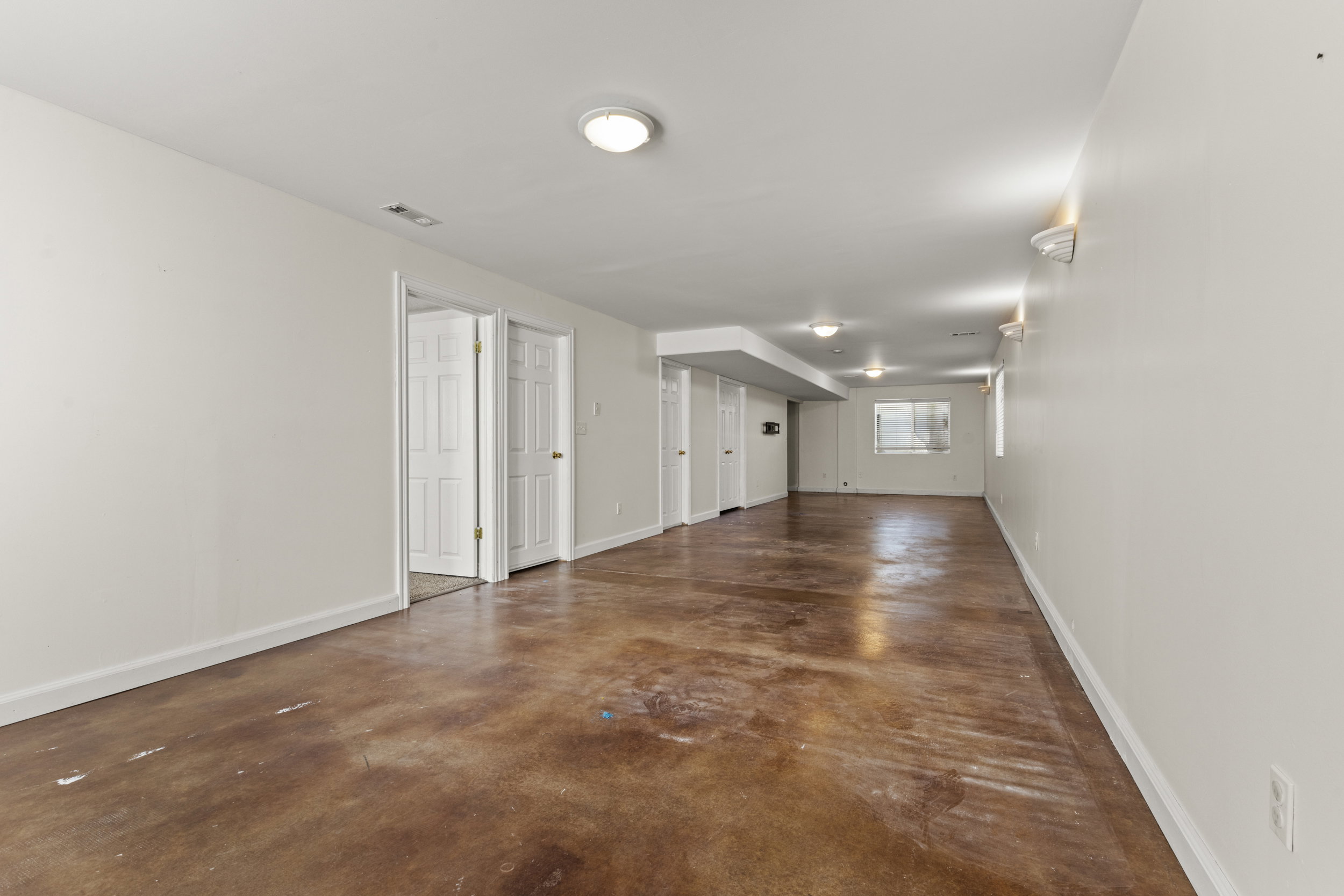 Expansive finished lower level featuring a stained concrete floor, white walls, multiple recessed light fixtures, and two panel doors