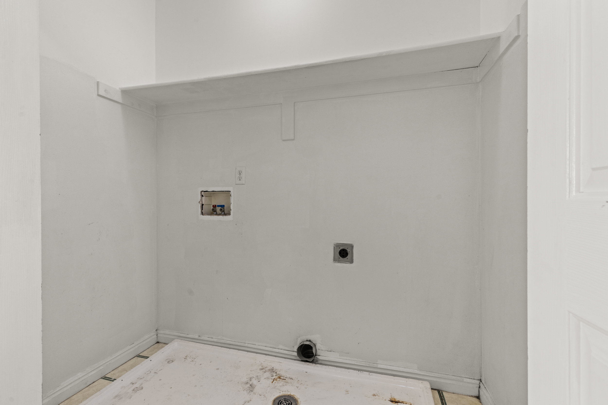 Dedicated utility area featuring a built-in shelf, plumbing hookups, and a floor drain