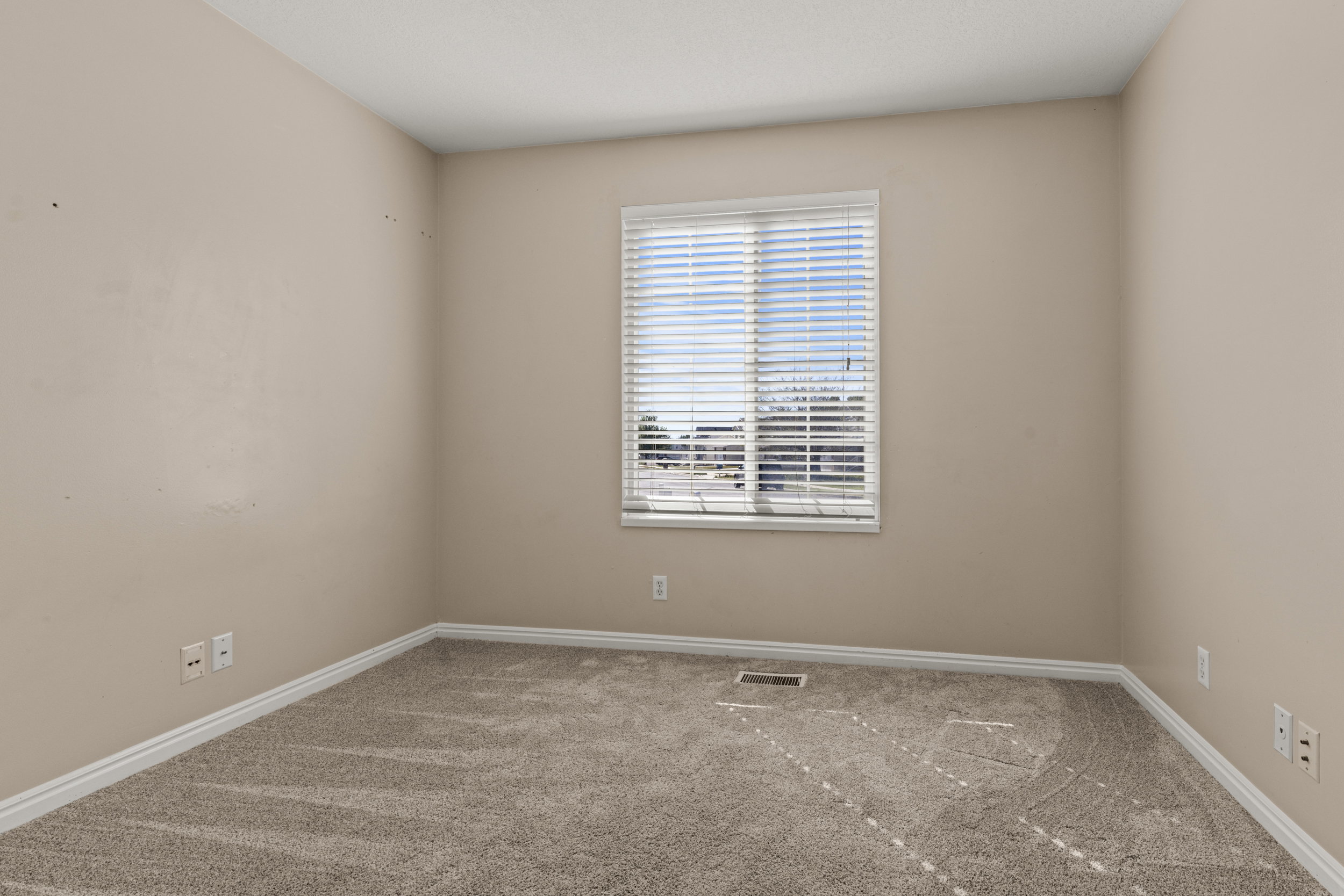 Neutral-toned interior room featuring a large window with horizontal blinds, providing natural illumination