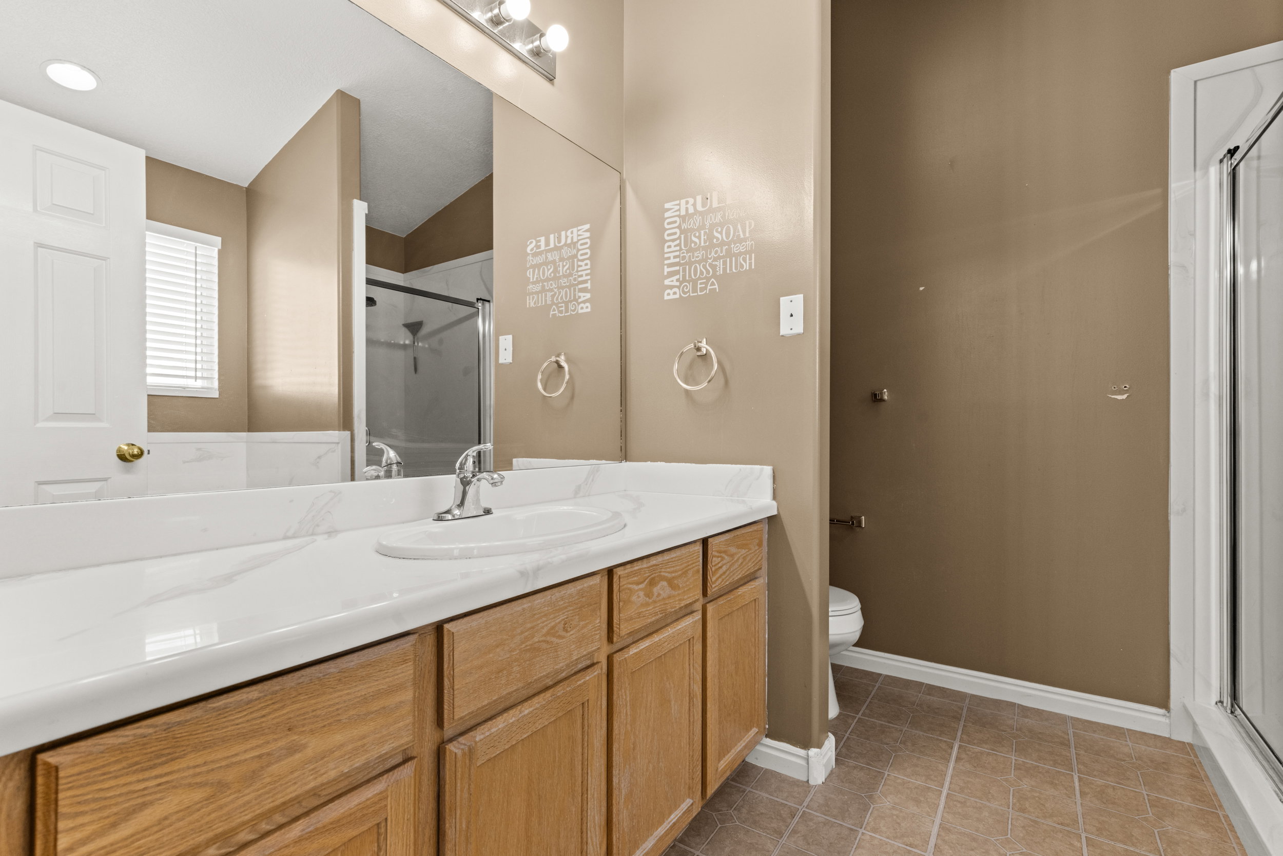Double vanity with integrated sink and chrome faucet, wood-finish cabinetry, a large wall-mounted mirror, and tile flooring