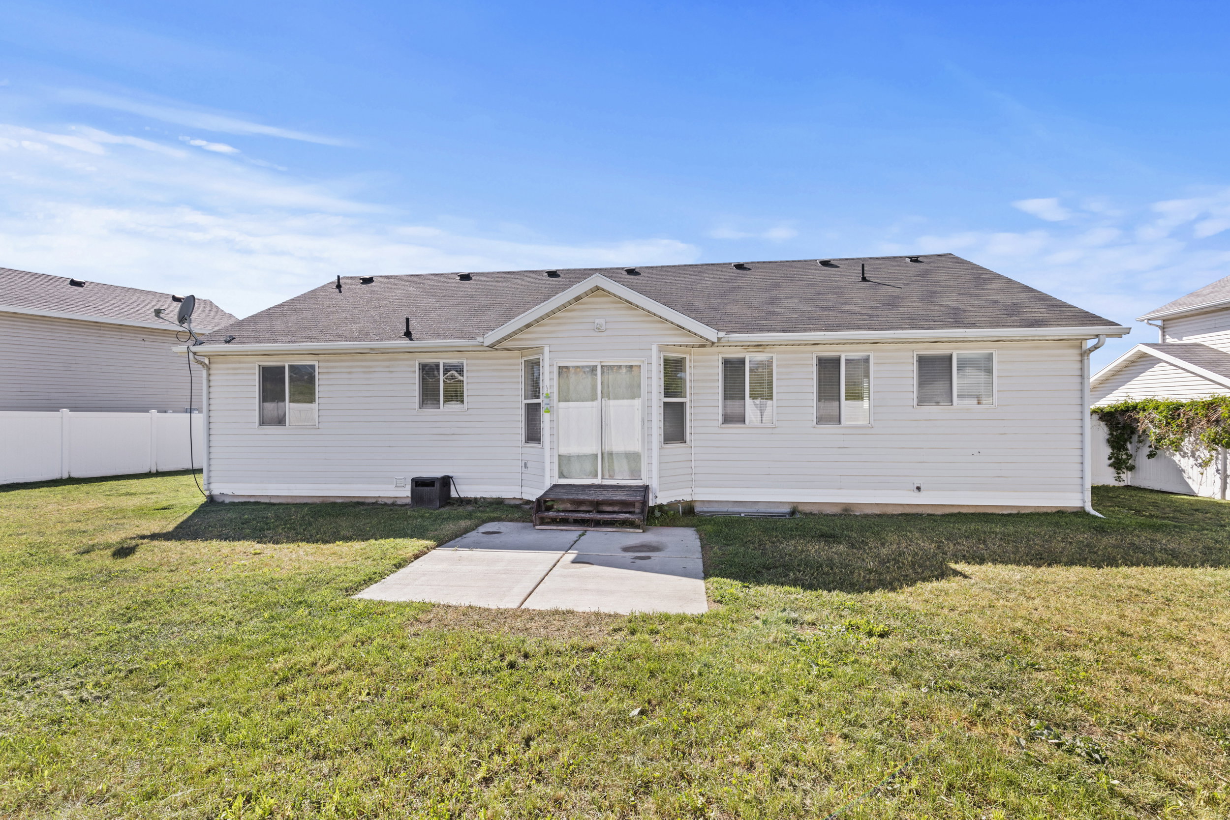 Expansive rear yard featuring a manicured lawn, concrete patio, and white vinyl siding