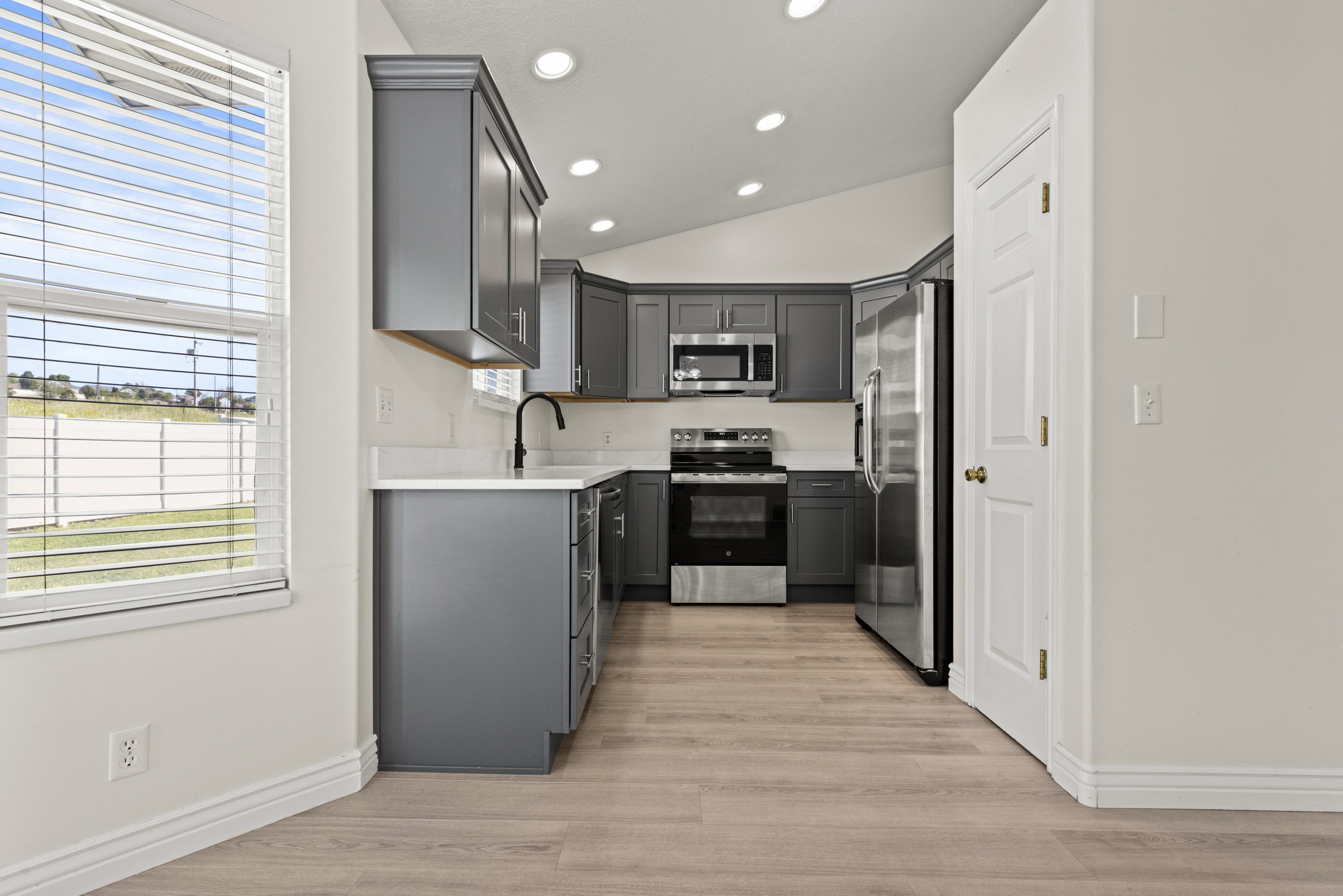 Modern kitchen featuring gray cabinetry, stainless steel appliances, light-toned countertops, and wood-finish flooring