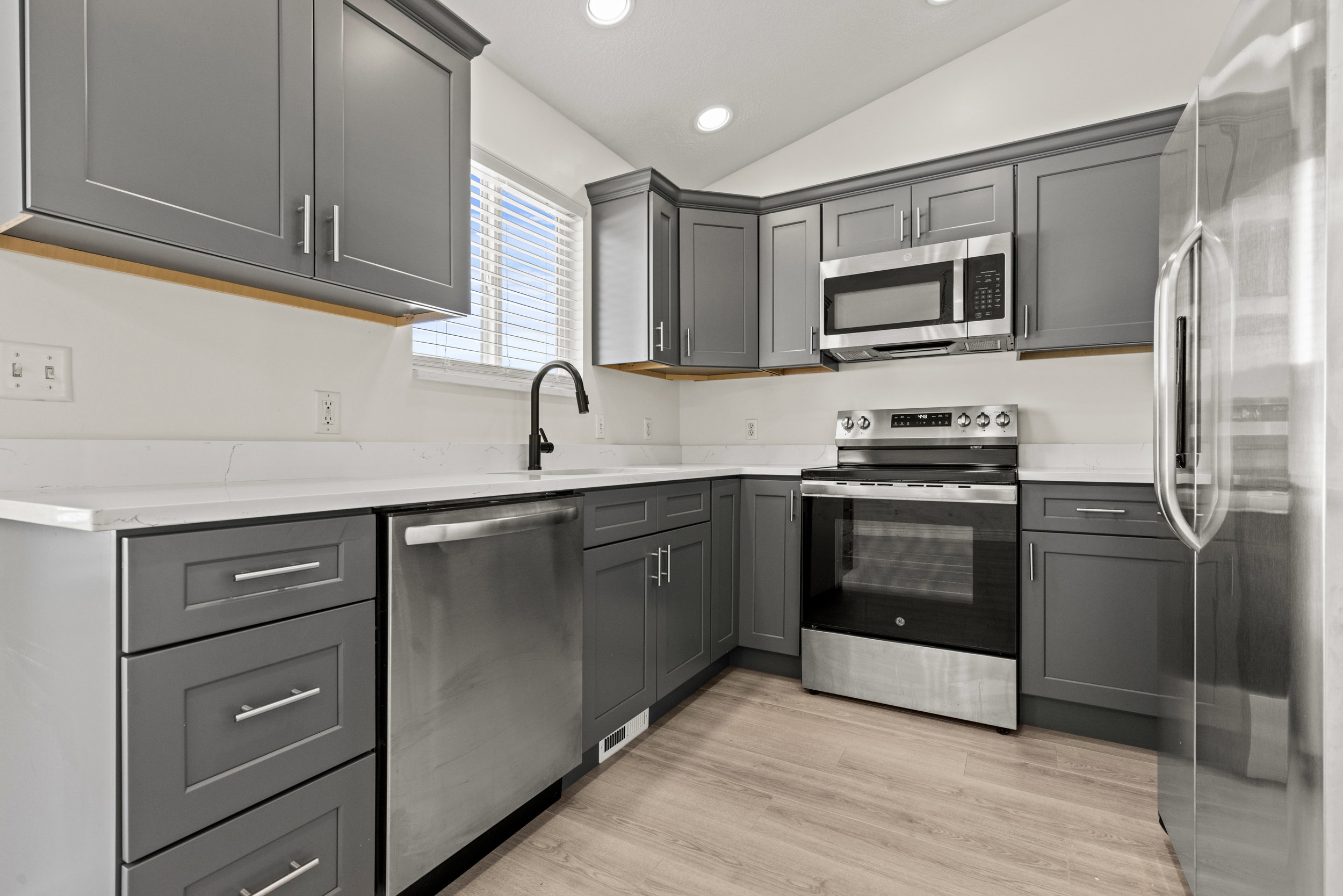 Modern kitchen featuring grey shaker-style cabinetry, white countertops, and stainless steel appliances