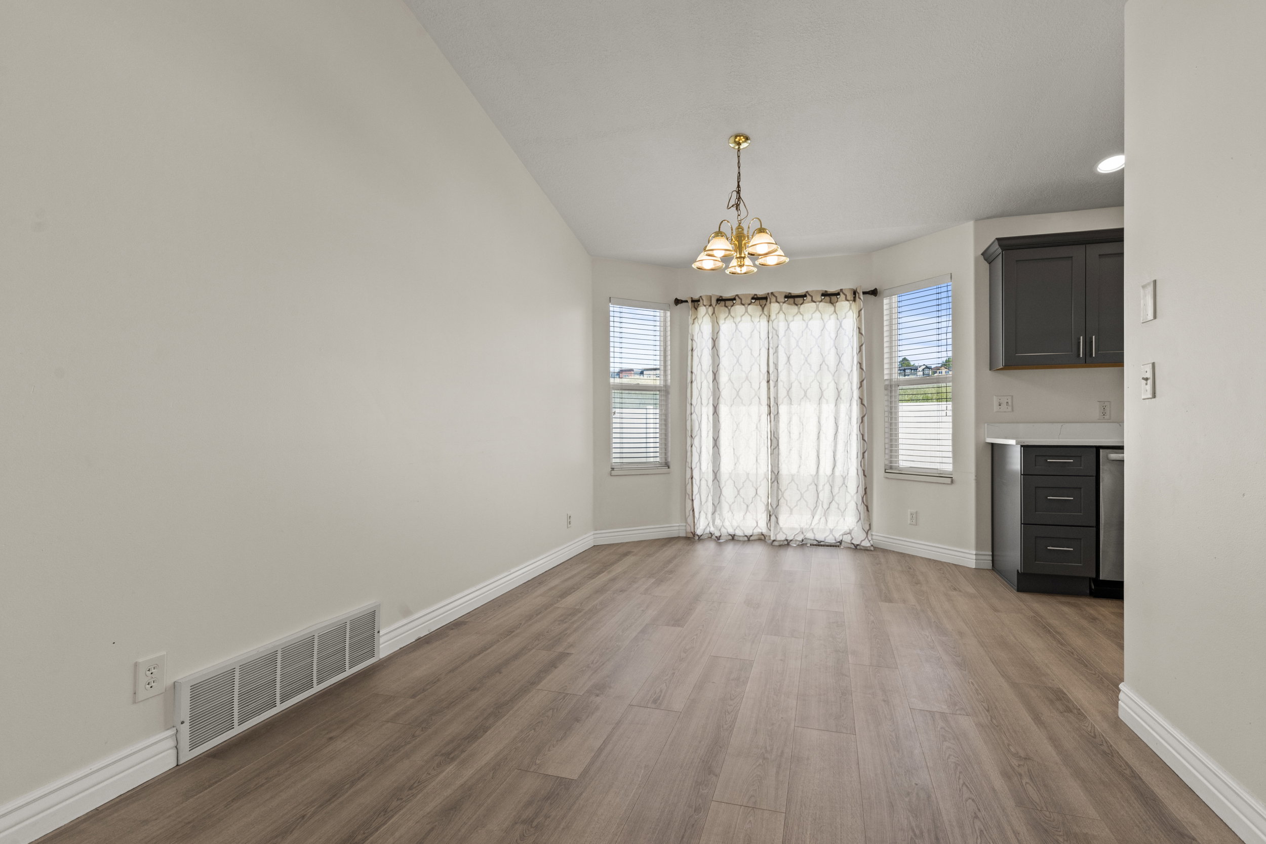 Open-concept space featuring wood-finish flooring, a bay window with vertical blinds, and a gold-toned chandelier