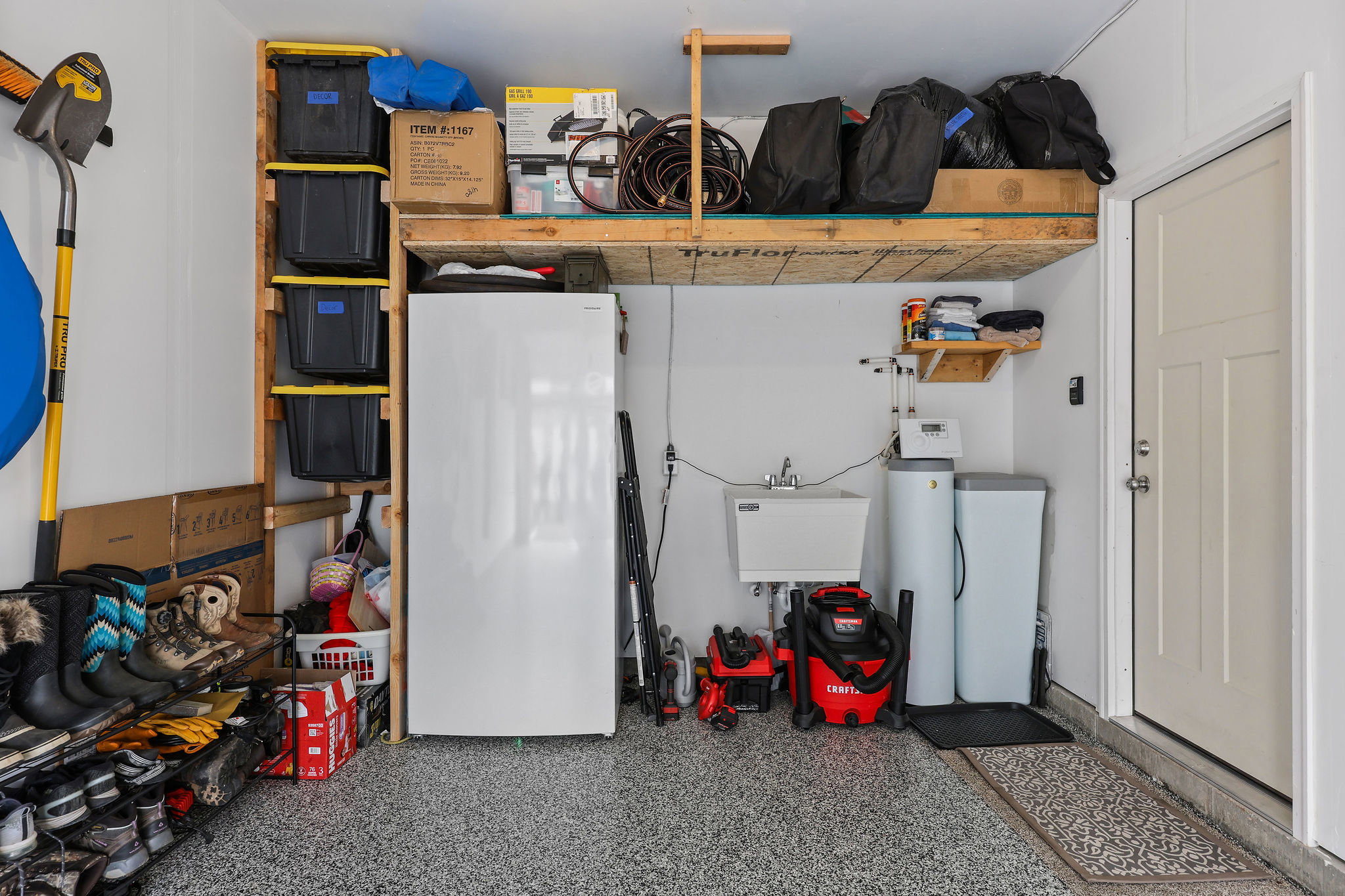 Garage featuring an epoxy-coated concrete floor, overhead storage shelving, a utility sink, and installed water filtration systems