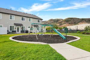 Community playground featuring a swing set and slide on a mulch ground cover, surrounded by manicured green space