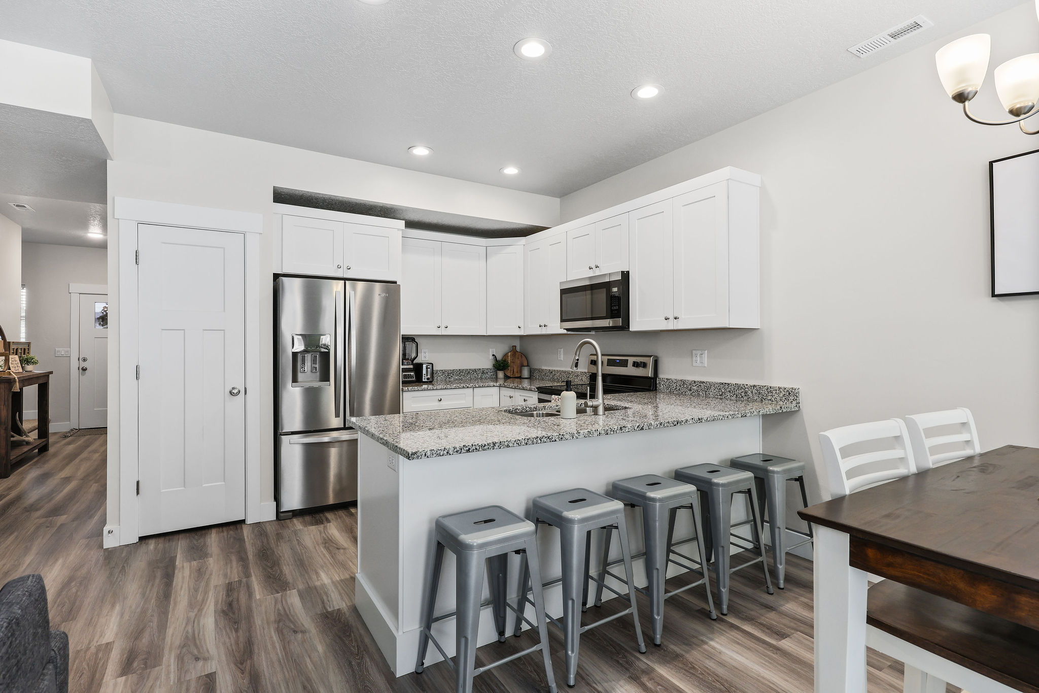 Kitchen featuring white cabinetry, stainless steel appliances, a granite countertop island with seating, and wood-finish flooring