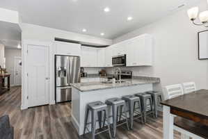 Kitchen featuring white cabinetry, stainless steel appliances, a granite countertop island with seating, and wood-finish flooring