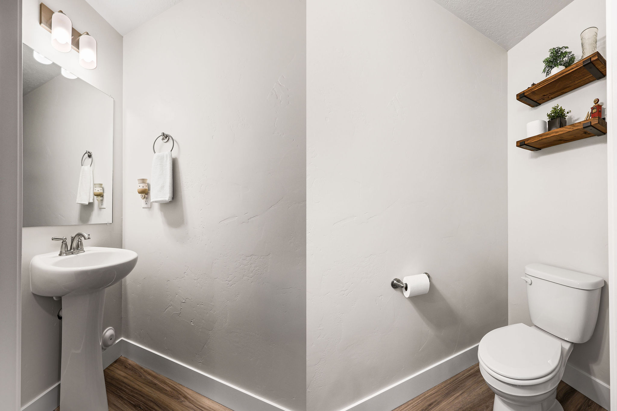 Pedestal sink with chrome faucet, wall-mounted mirror, and overhead vanity lighting