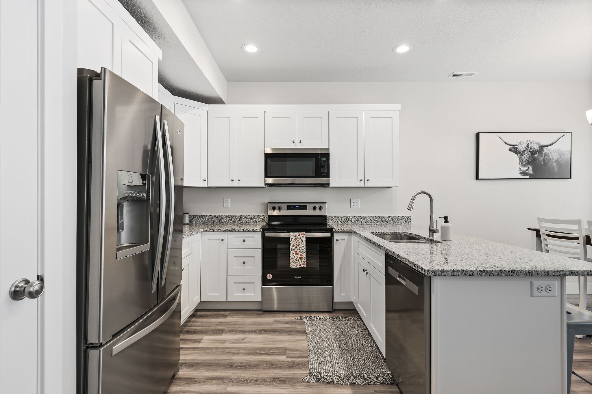 Kitchen featuring white cabinetry, stainless steel appliances, granite countertops, wood-finish flooring, and recessed lighting