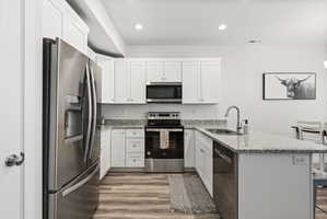 Kitchen featuring white cabinetry, stainless steel appliances, granite countertops, wood-finish flooring, and recessed lighting