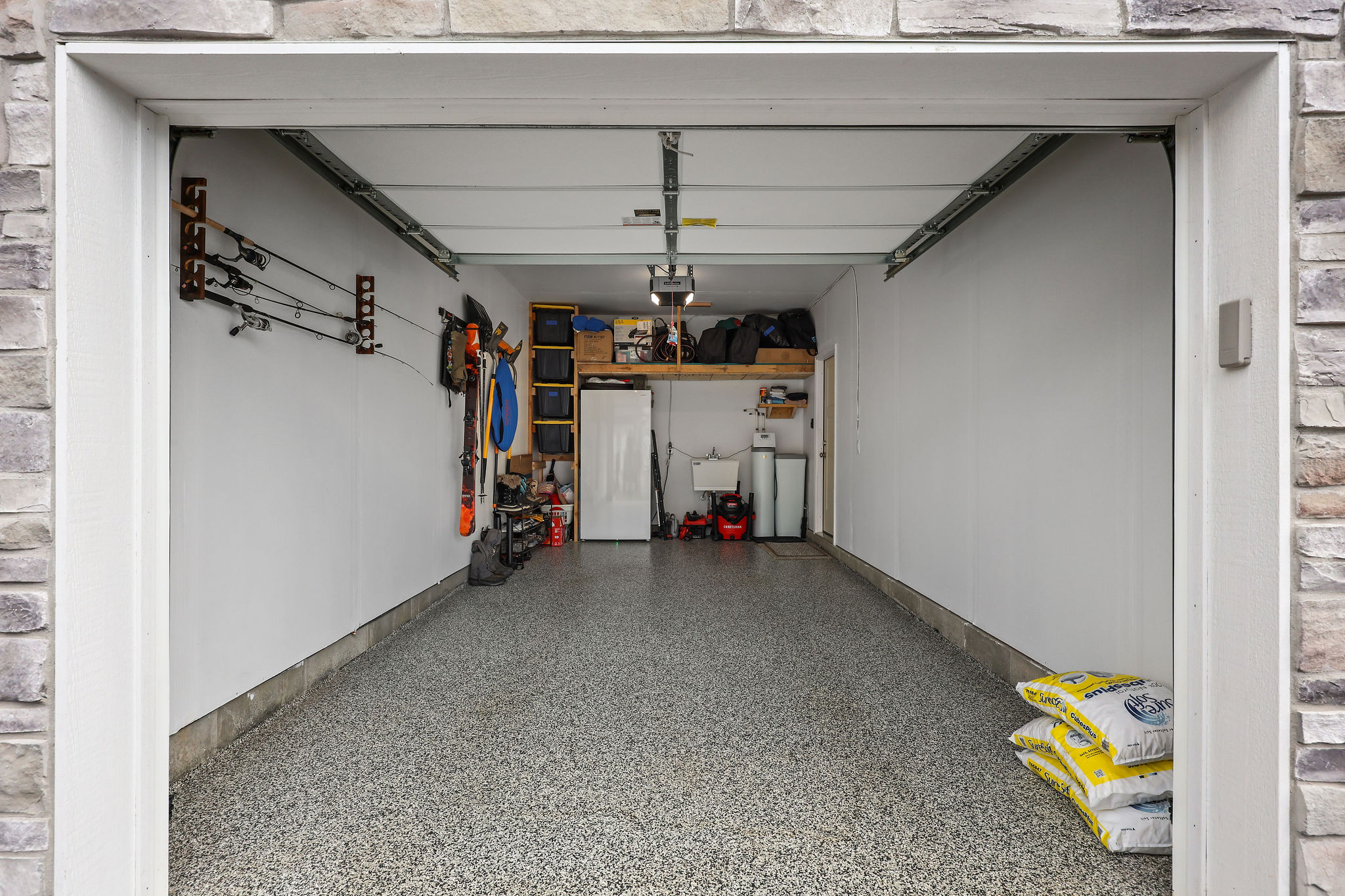Spacious garage featuring stone-clad exterior entry, durable epoxy flooring, and ample overhead storage shelving