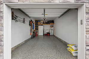 Spacious garage featuring stone-clad exterior entry, durable epoxy flooring, and ample overhead storage shelving