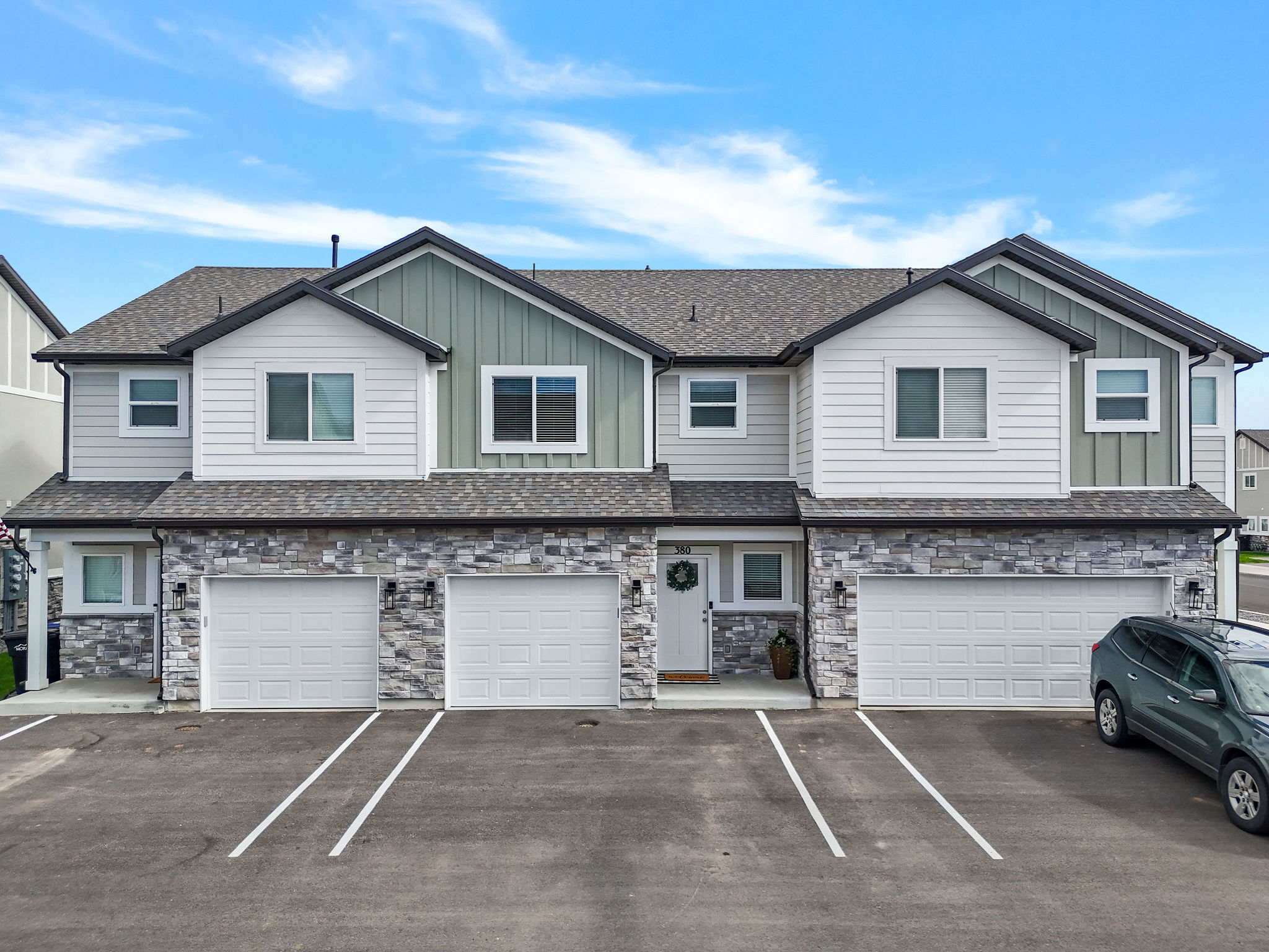 Modern townhome exterior featuring stone accents, light gray siding, and green vertical siding elements